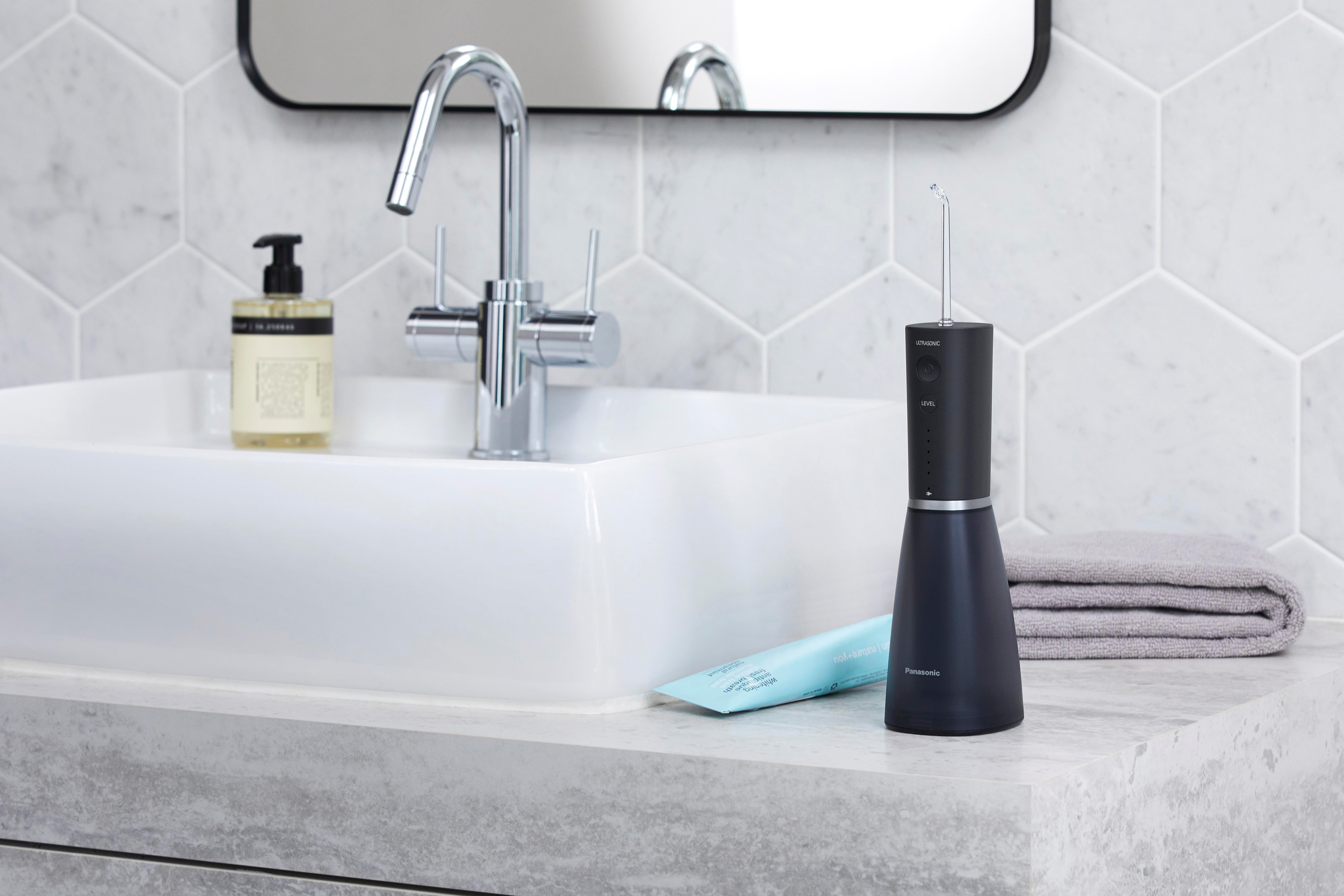 Badezimmer-Szene: ein weißes Waschbecken mit einer Chromarmatur, einem schwarzen Munddusche und einem Handtuch.