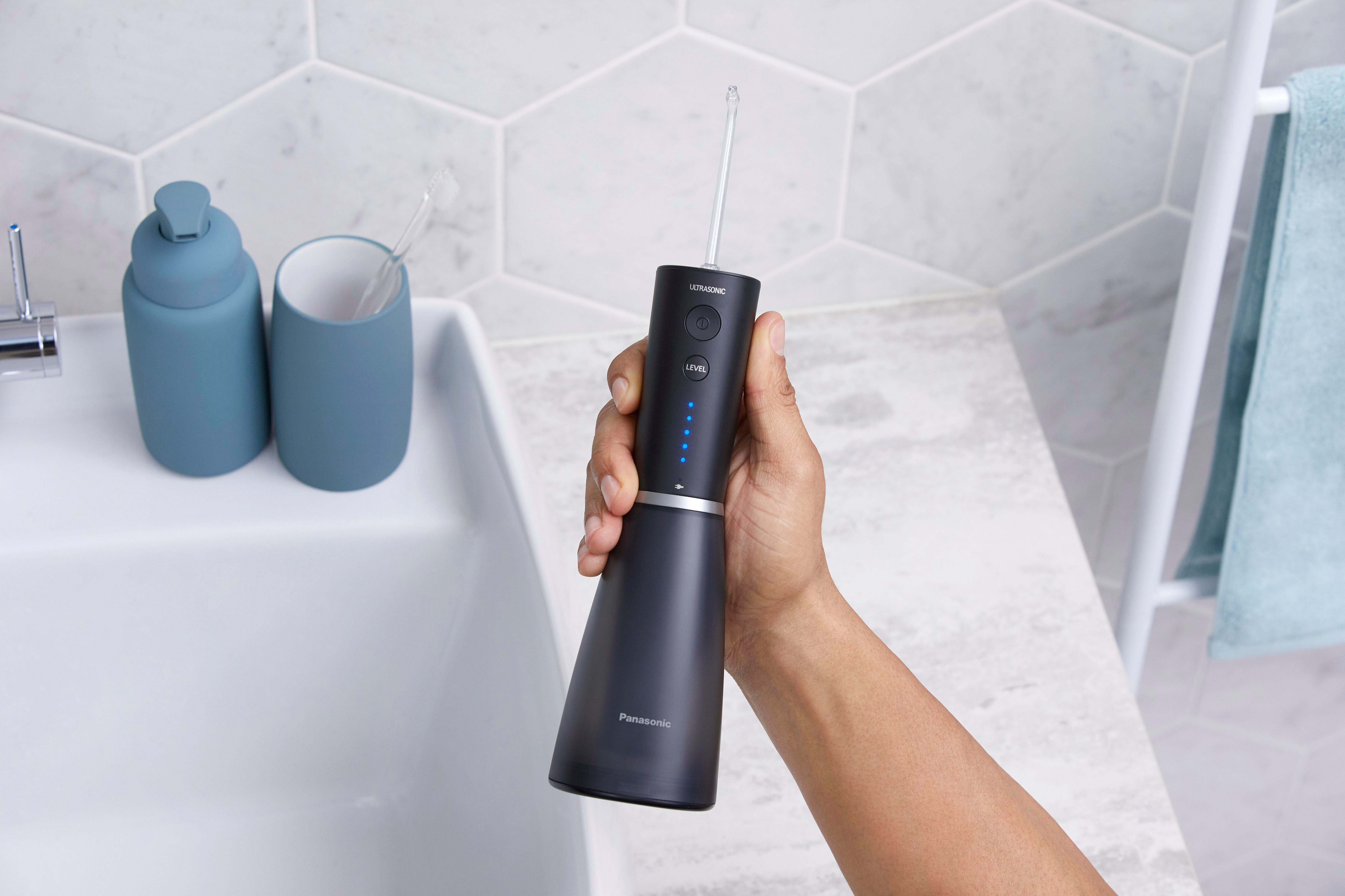 Hand hält schwarzen Panasonic-Wasserflosser in der Nähe eines Waschbeckens.