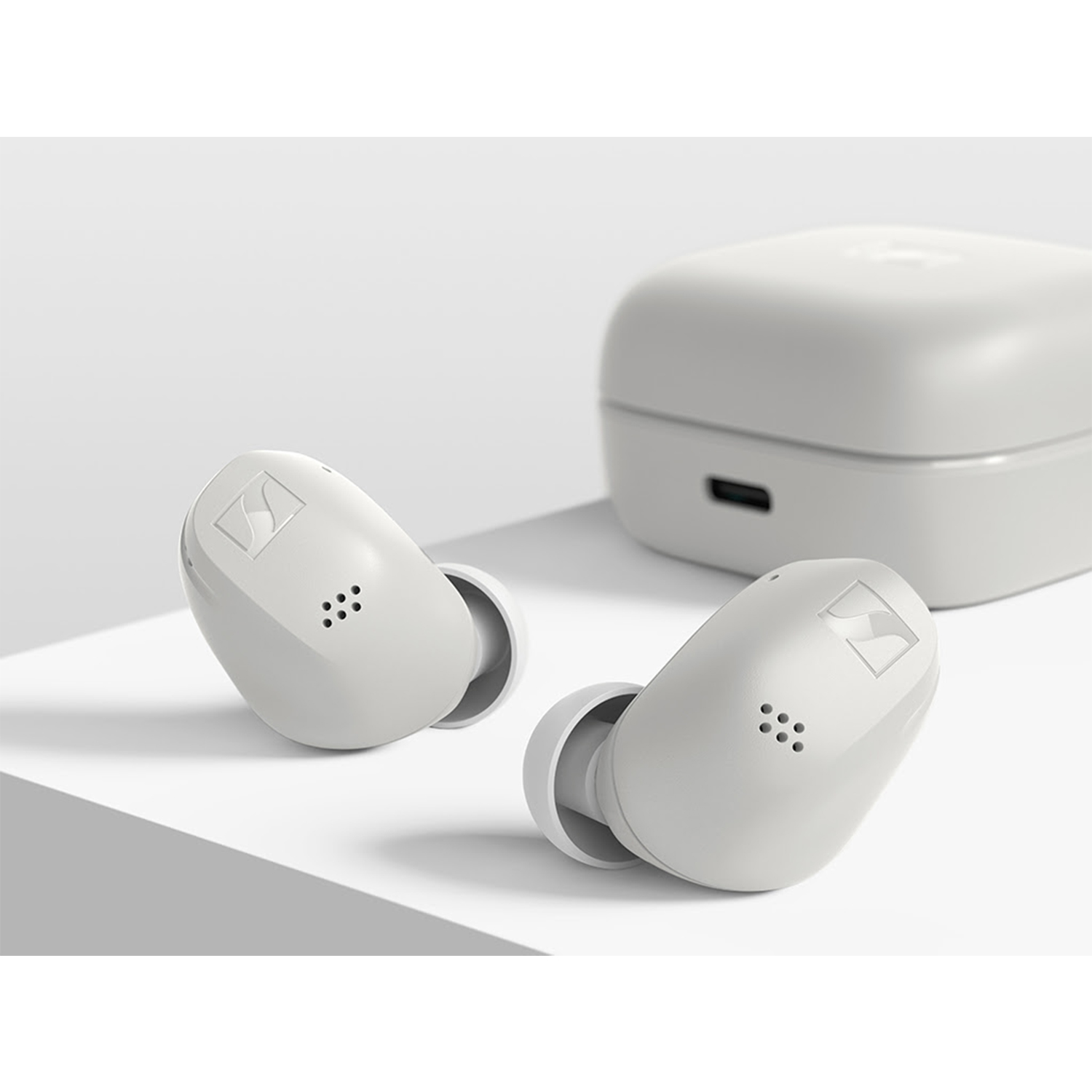 Auricolari wireless bianchi con custodia di ricarica su superficie bianca. Logo Sennheiser visibile.