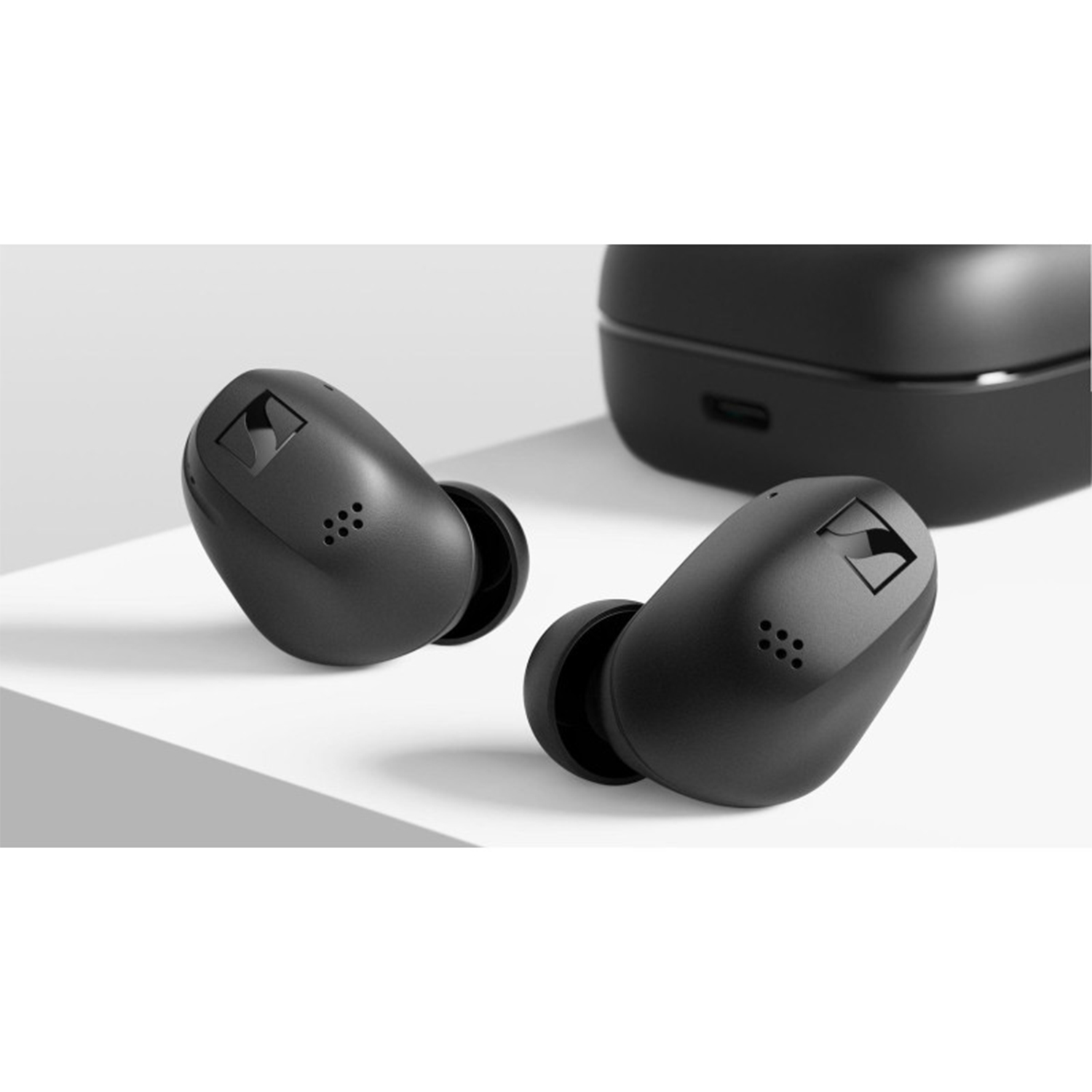Due auricolari neri e un astuccio di ricarica nero su una superficie bianca. Gli auricolari sono angolati verso lo spettatore.