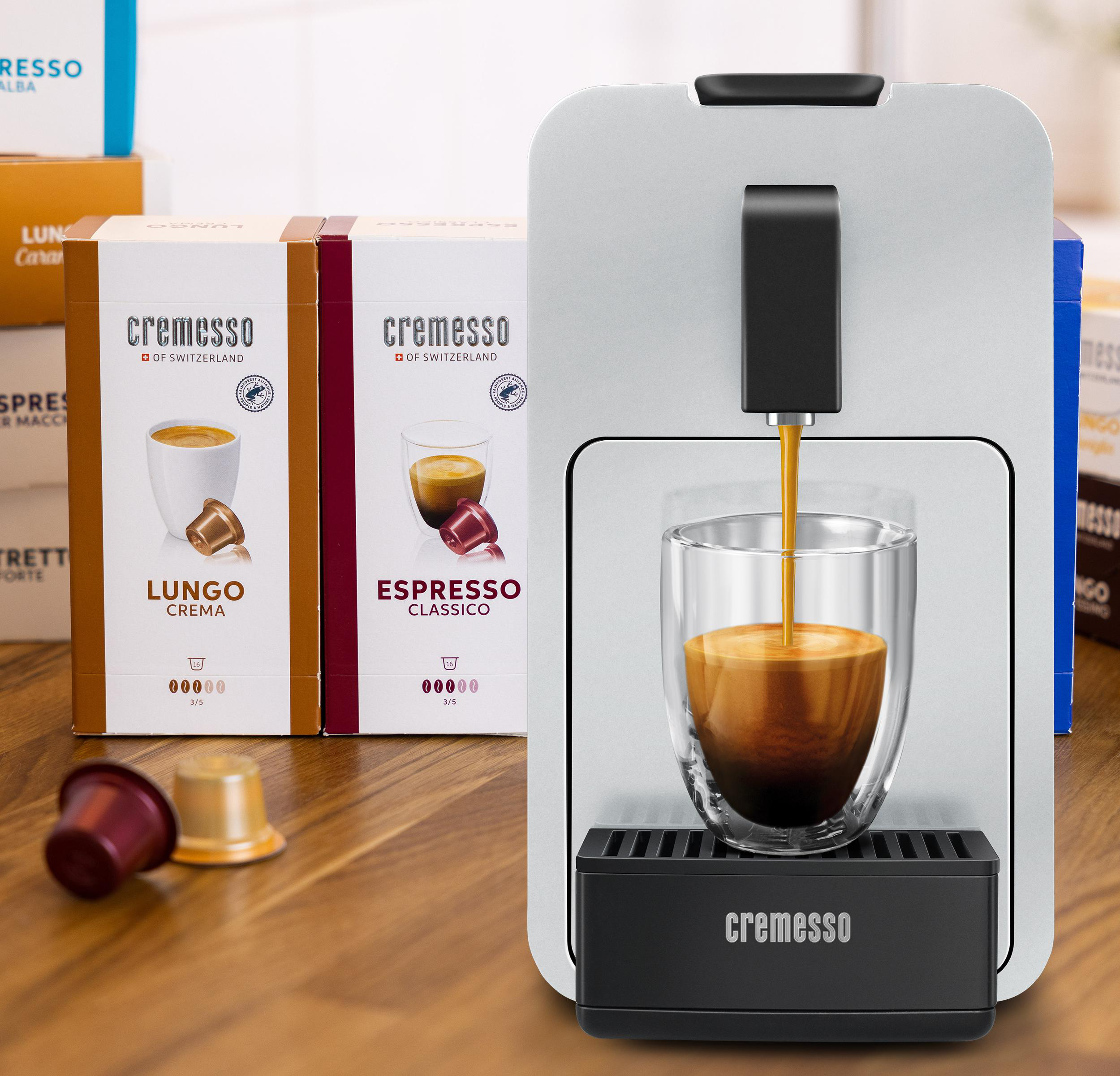 Kaffeemaschine, die Kaffee in ein Glas ausgibt. Zwei Kisten mit Kaffeekapseln. Text: Cremesso Kaffee.