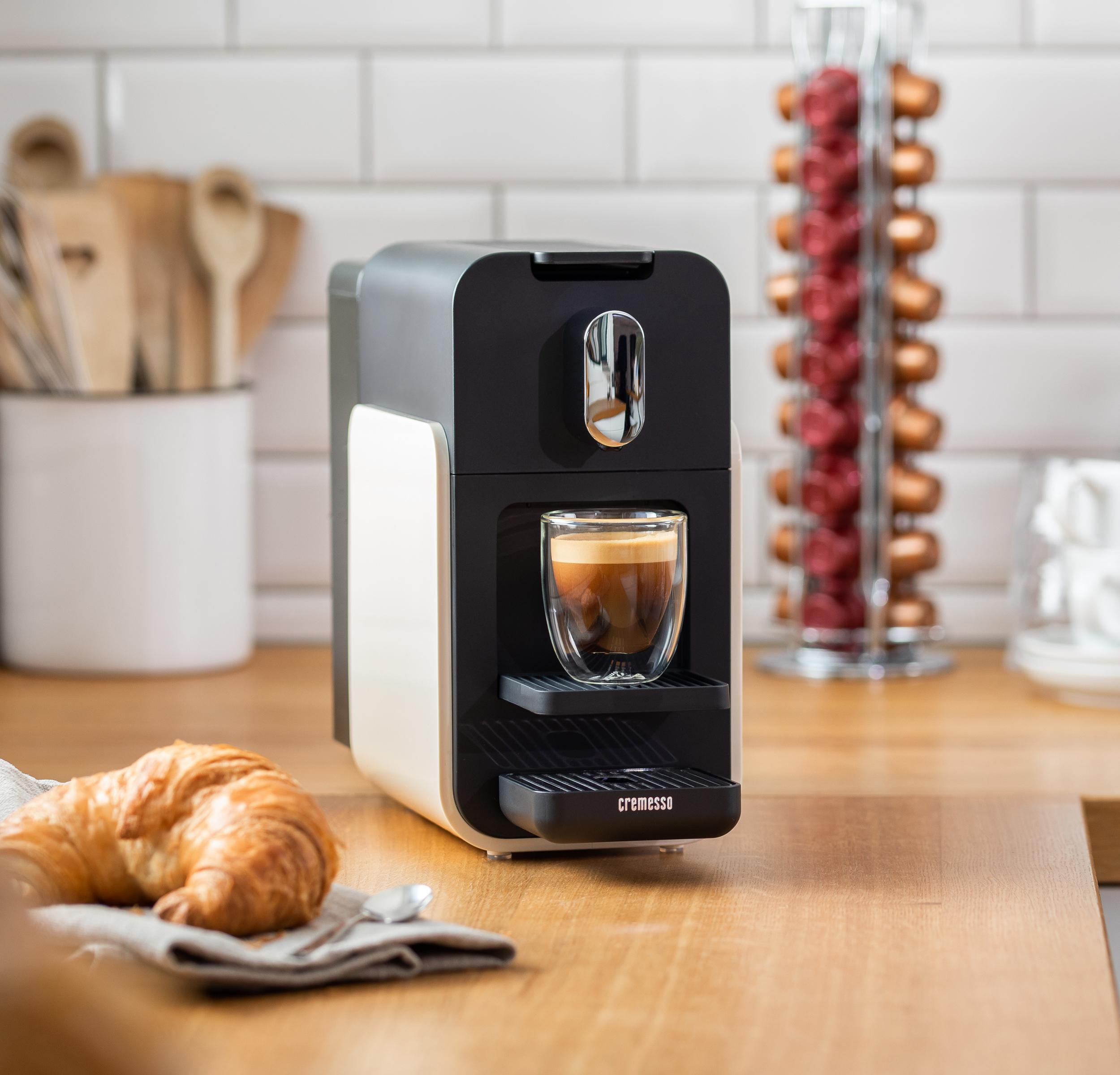 Kaffeemaschine, Tasse mit Kaffee, Croissant und Kapselhalter auf Holzoberfläche.