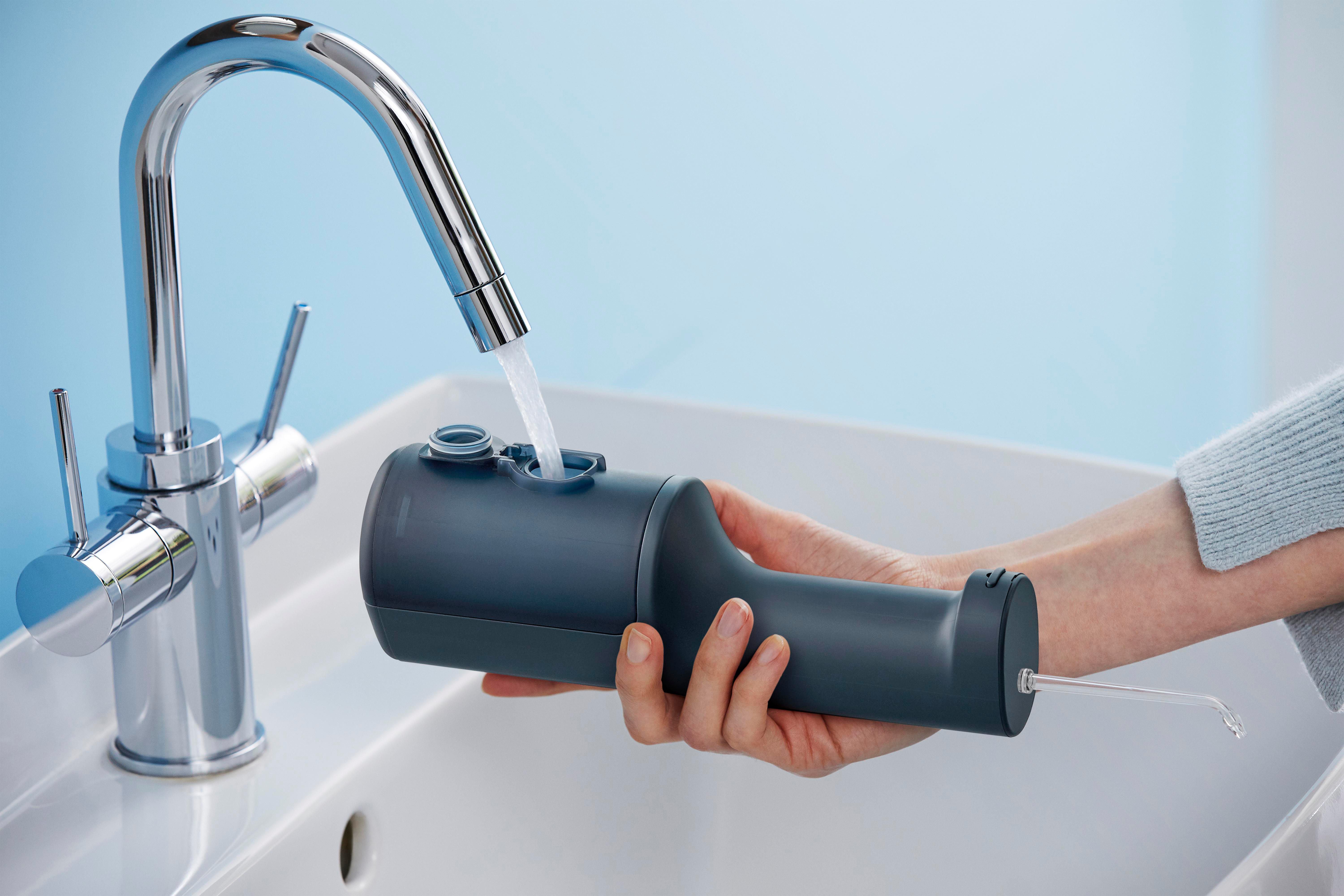 Person befüllt dunklen grauen Wasser-Flosser mit Wasser aus silbernem Wasserhahn.