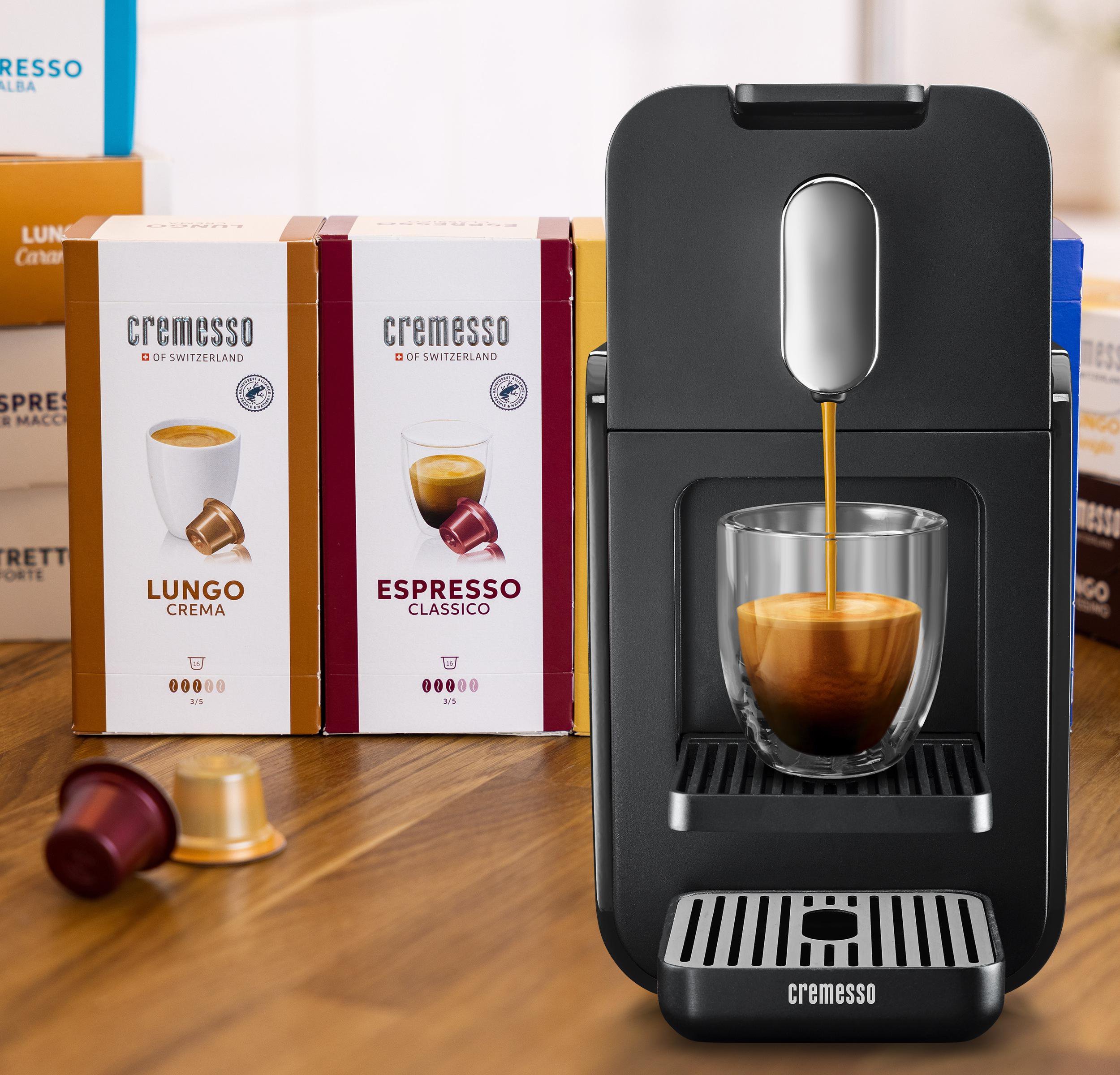 Schwarze Kaffeemaschine mit Kaffee, der in ein Glas gegossen wird. Zwei Kaffeeboxen im Hintergrund.