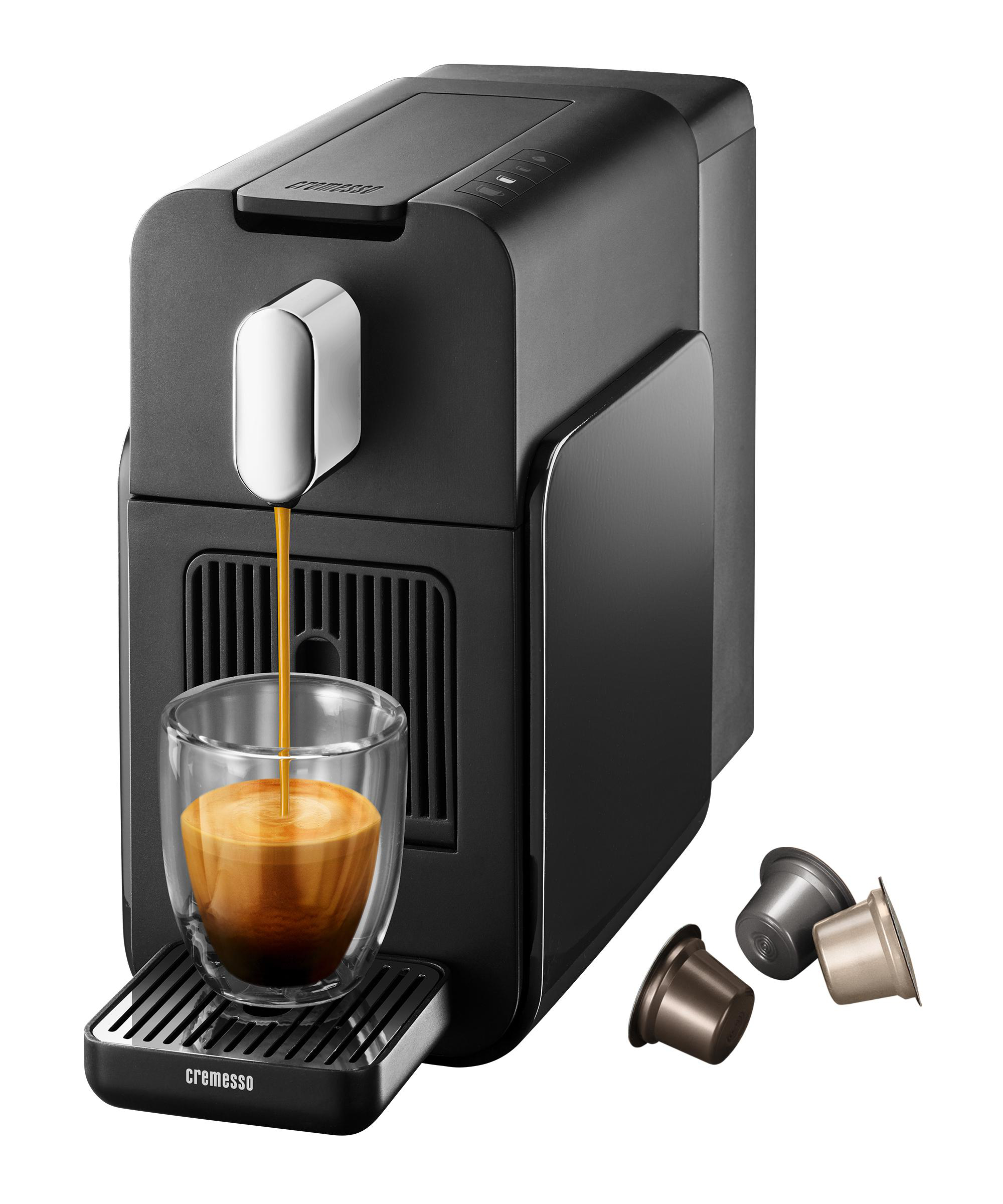 Eine schwarze Kaffeemaschine, die Kaffee in ein Glas gießt. Drei Kaffeekapseln daneben.