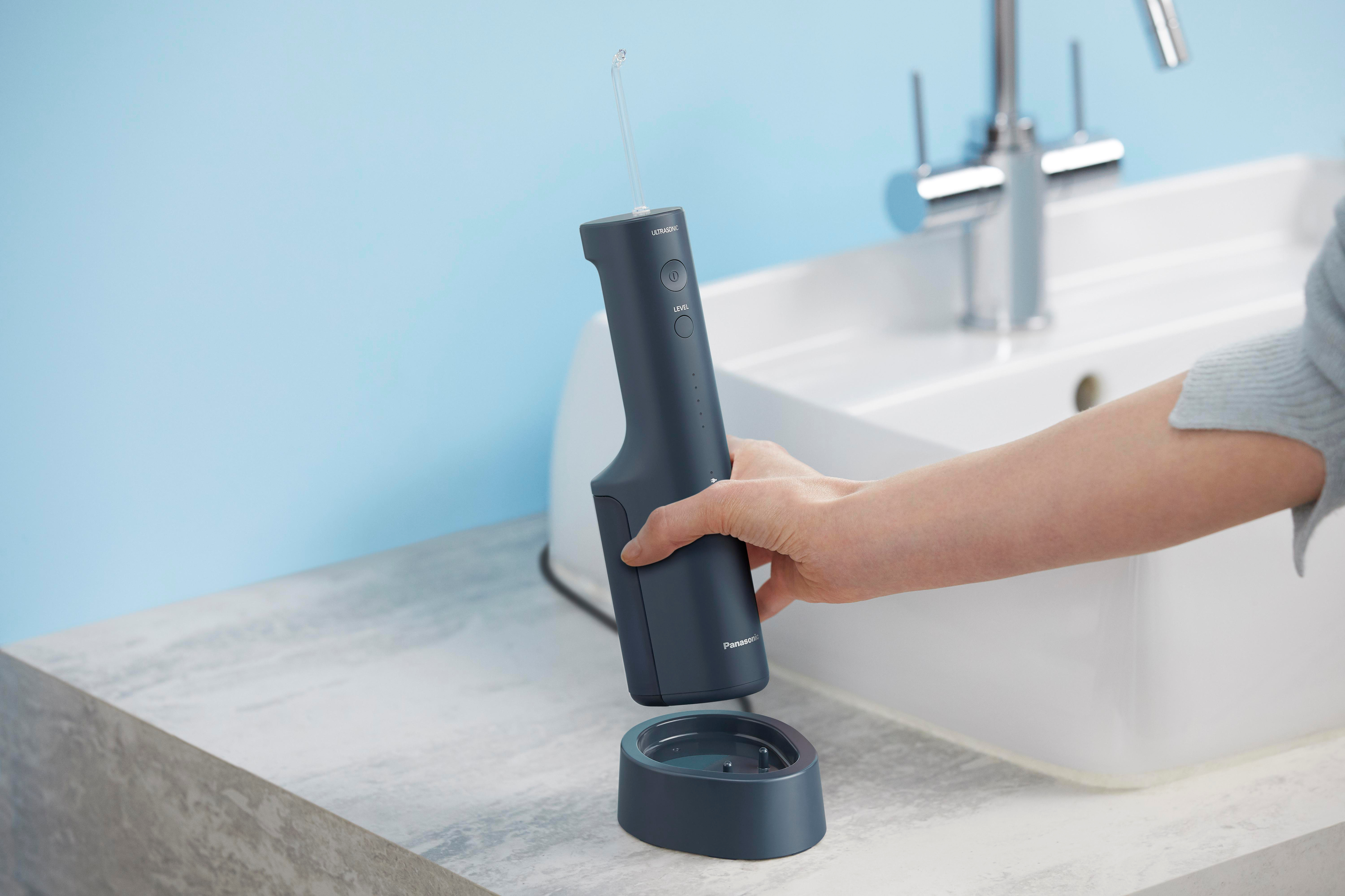 Hand platziert einen dunkelblauen Wasser-Flosser auf seiner Ladestation am Waschbecken.