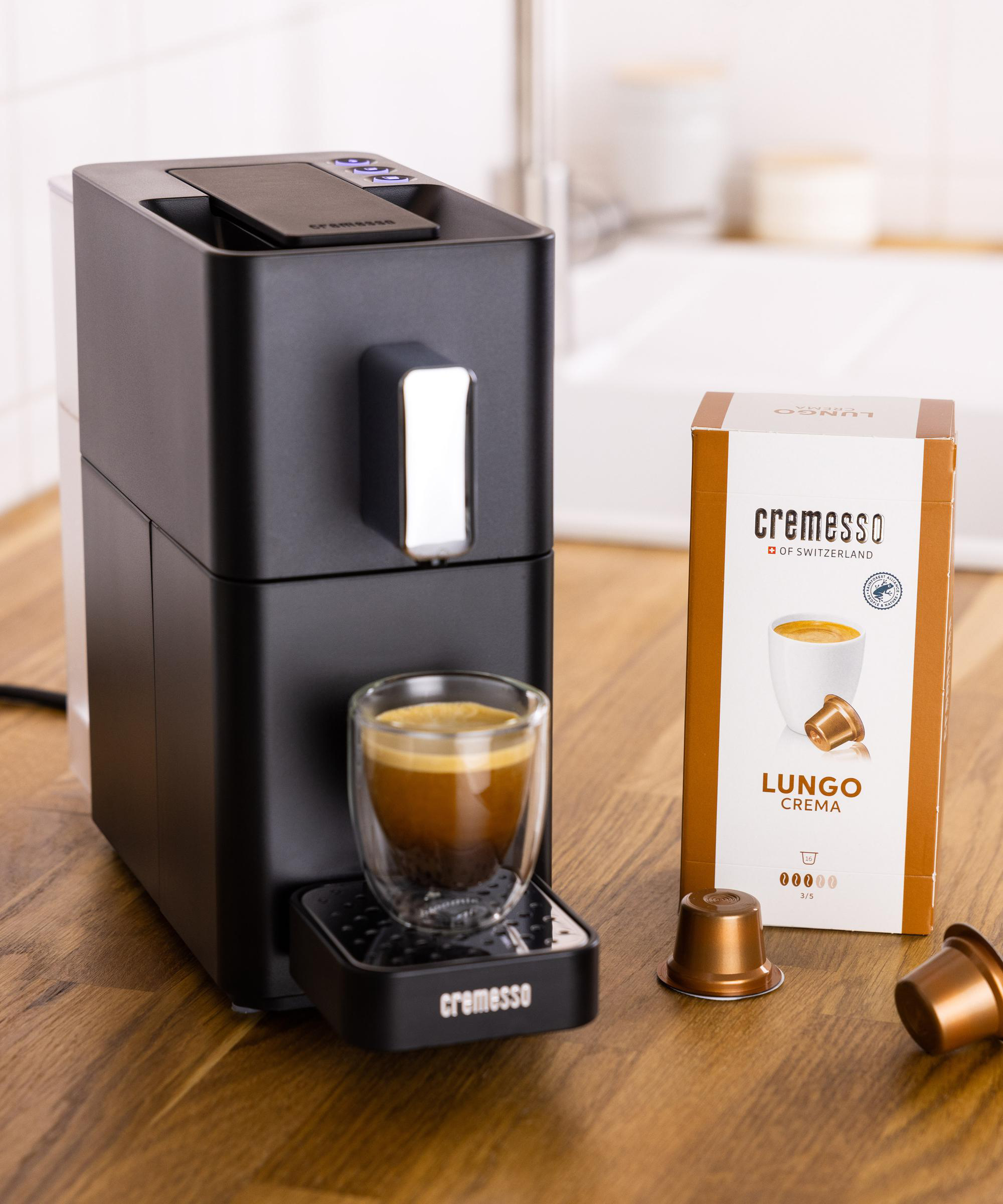 Espressomaschine mit Kaffeeglas, Kaffeepads und einer Schachtel. Holztisch.