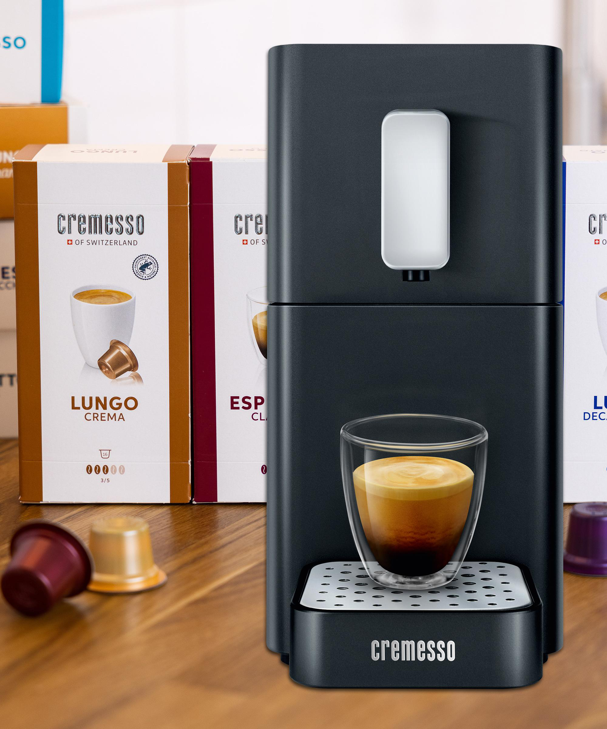 Espressomaschine mit einem Glas Kaffee und Kapseln. Kartons im Hintergrund.