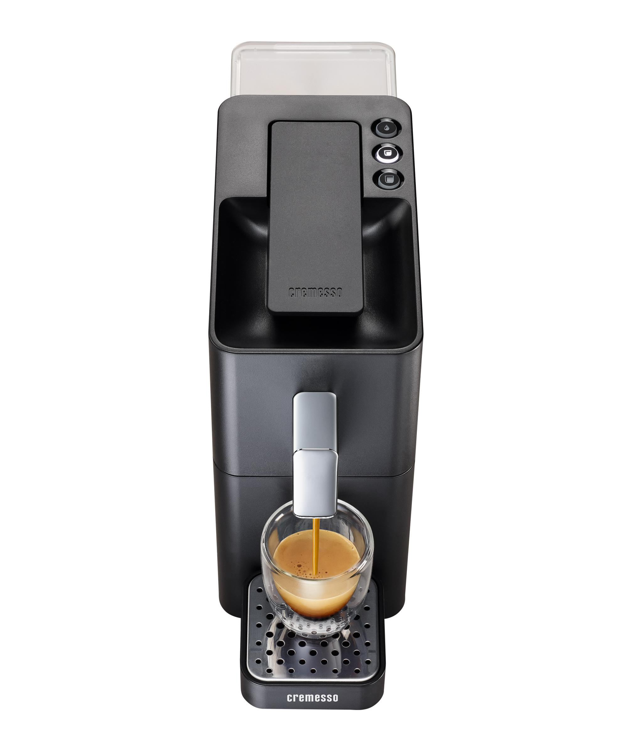 Eine schwarze Kaffeemaschine, die Kaffee in eine Glastasse auf einem Metallrost ausgibt, mit transparentem Deckel oben.