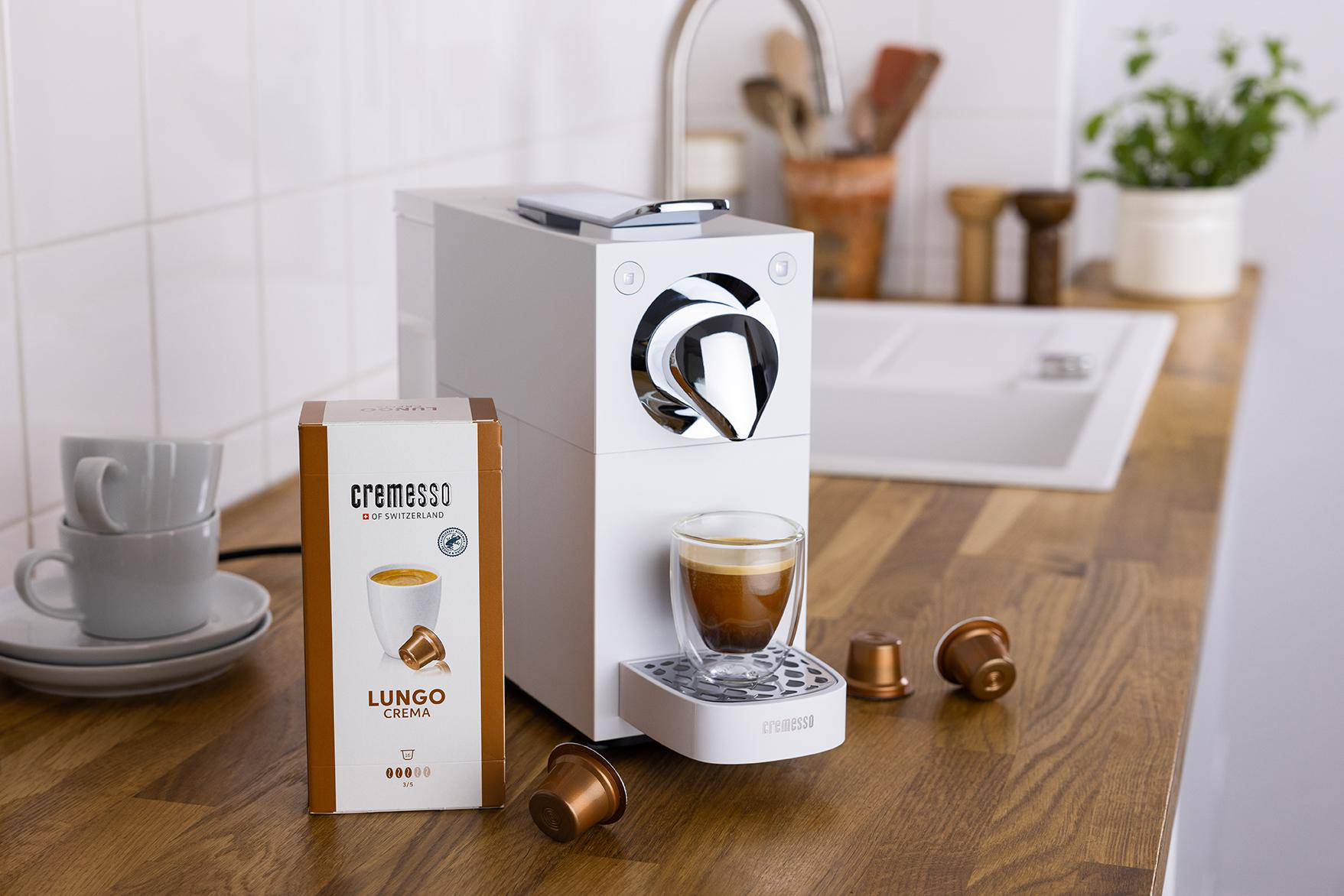 Weiße Kaffeemaschine mit einer Tasse Kaffee, die eingegossen wird. Kaffeepads links.