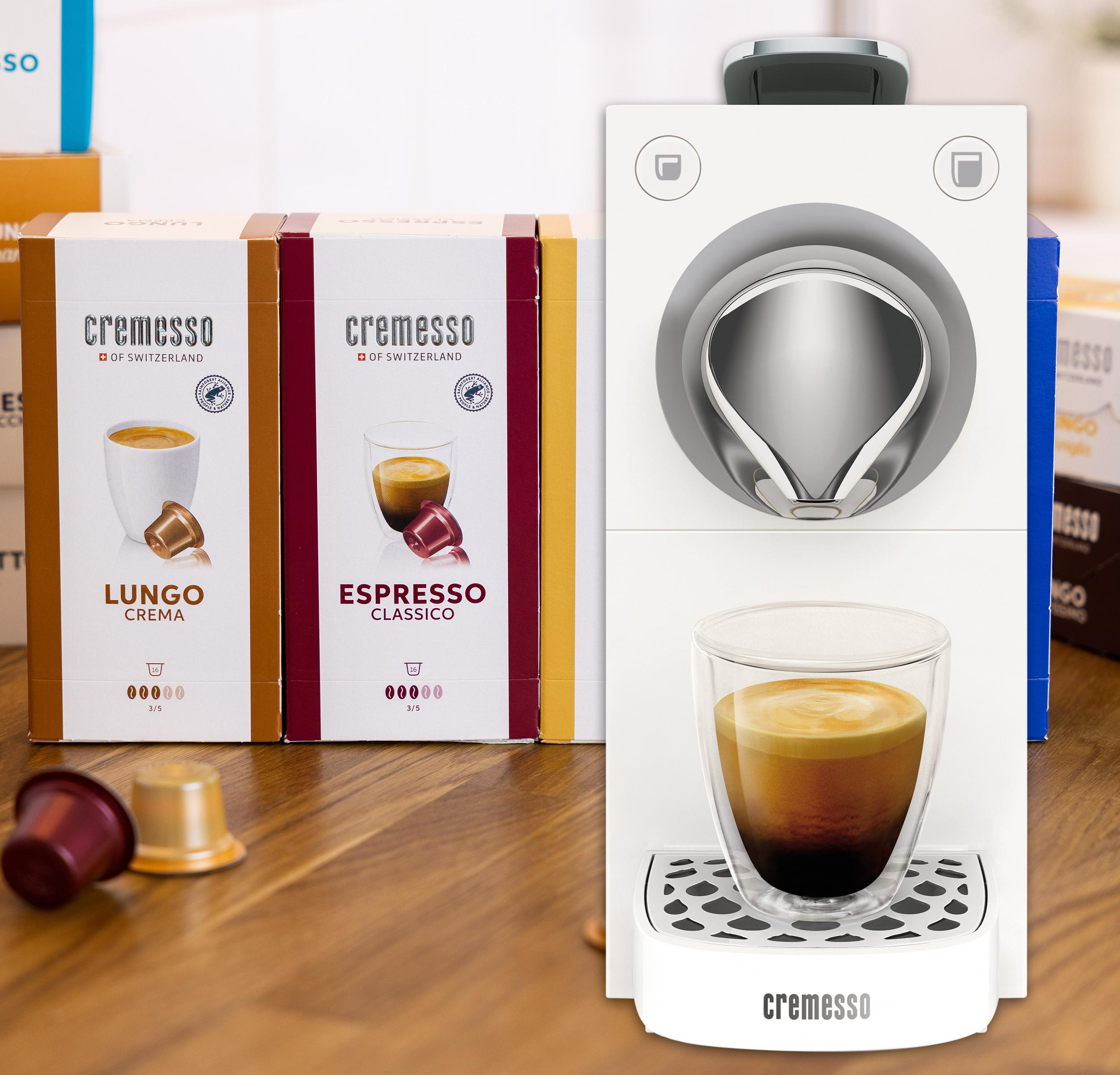 Espressomaschine mit Kaffee, Kapseln und Kartons. Glas mit Kaffee. Weiße Oberfläche.