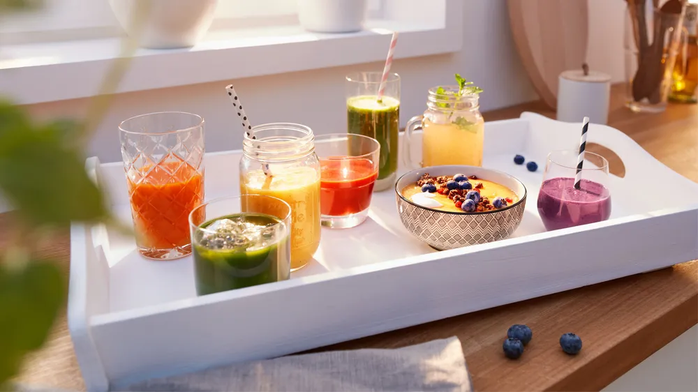 Fehér tálca színes italokkal és smoothie tál egy faasztalon.