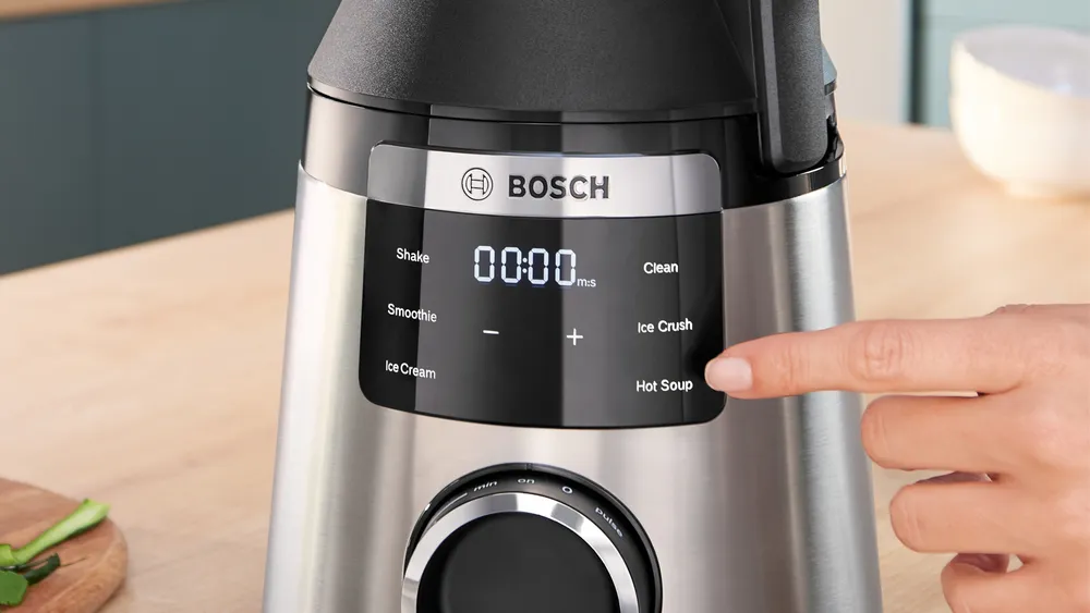 Egy turmixgép látható kijelzővel. Egy kéz a 'Hot Soup' gomb megnyomására készül.