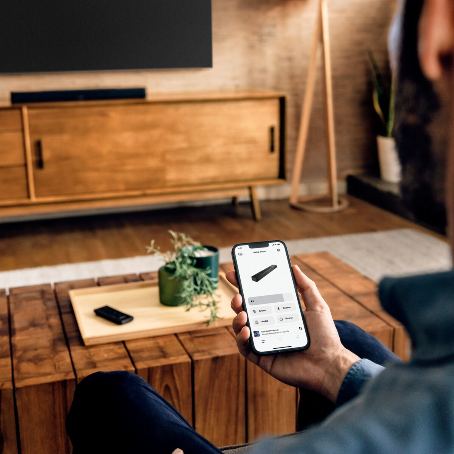 A person holding a smartphone with a control interface. Shows a sound bar, on a table.