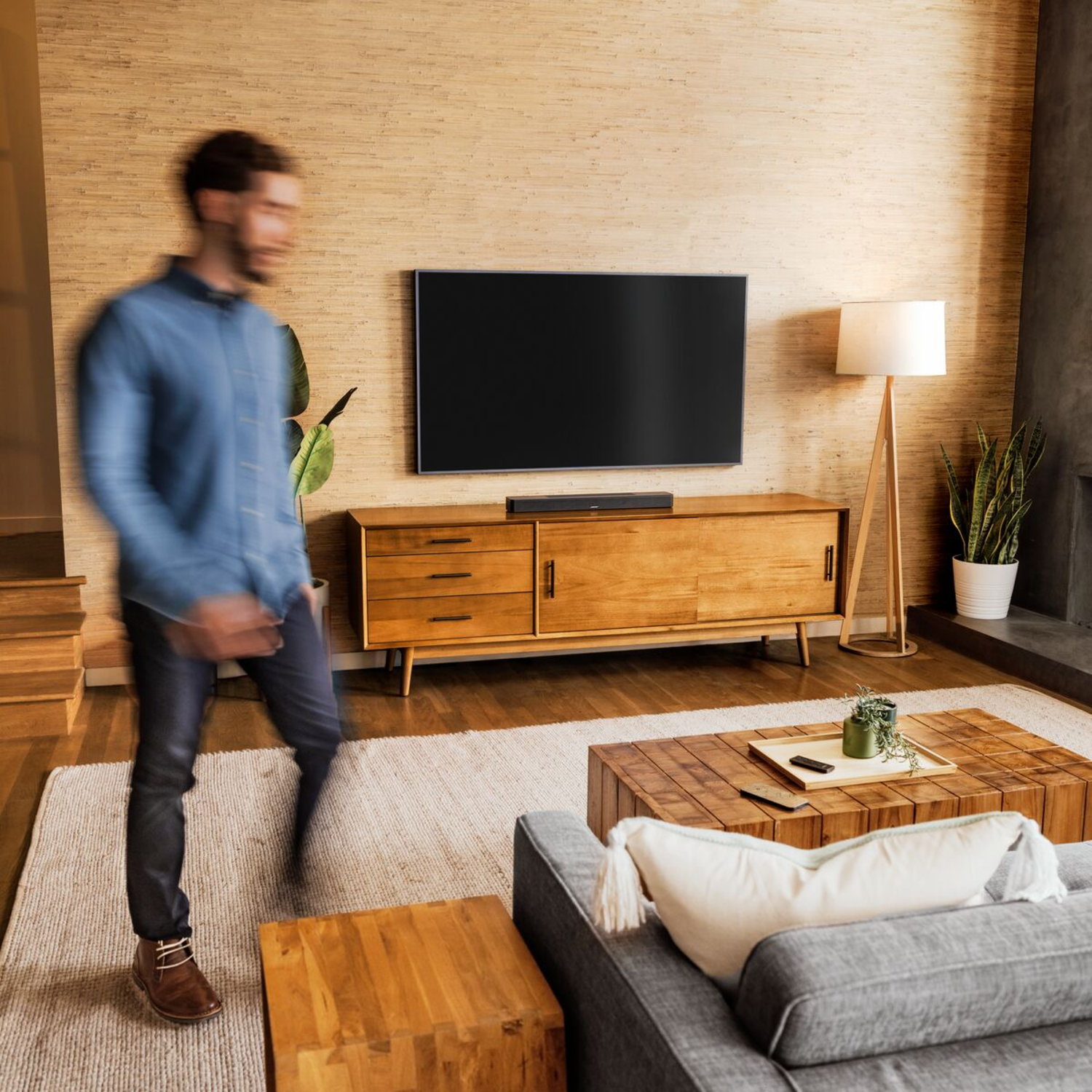 Living room scene: TV on wooden cabinet, lamp, sofa, and a person walking in the foreground.