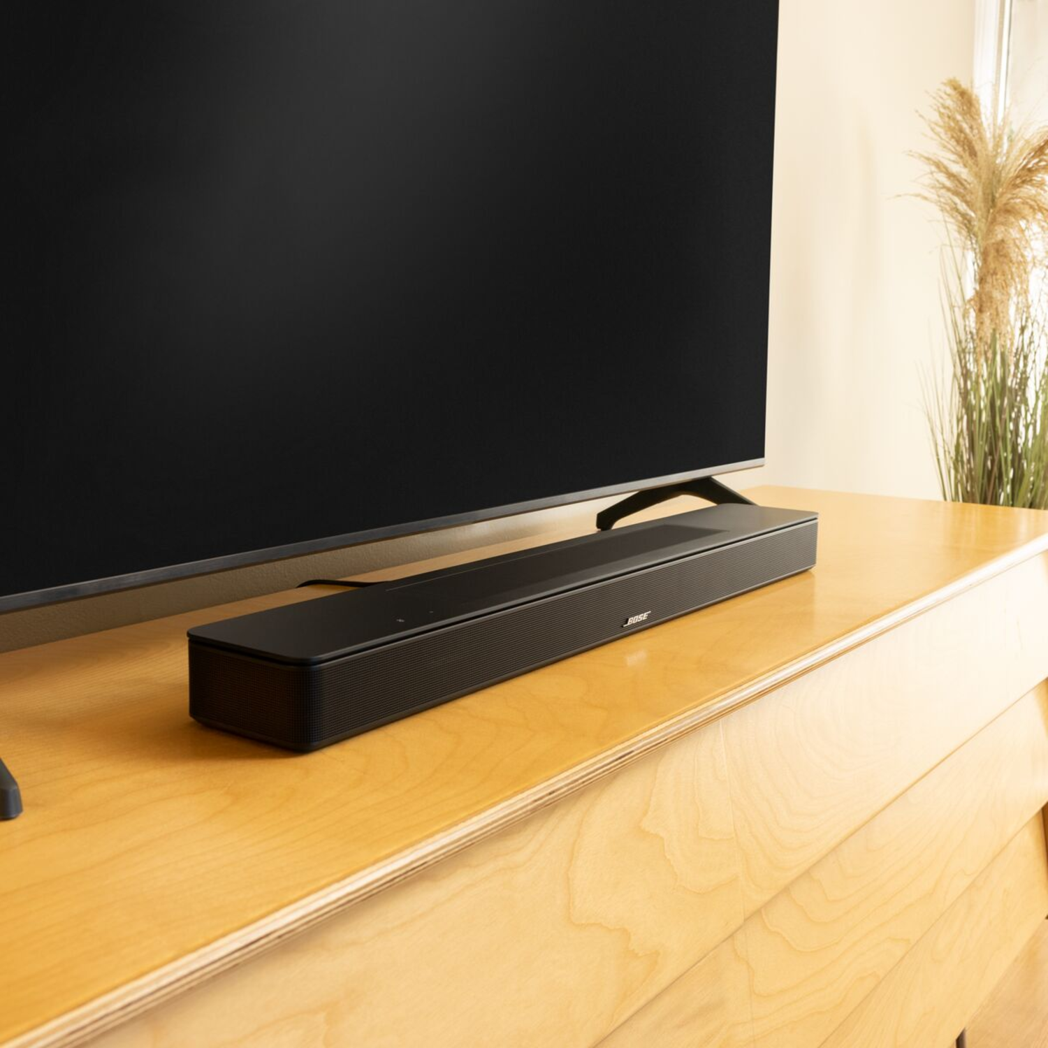 A black sound bar on a wooden cabinet below a large black television.