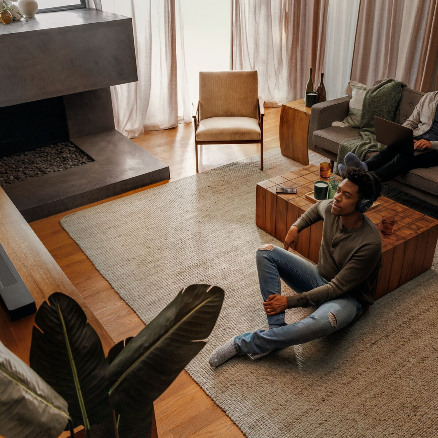Overhead shot of a living room. A person is seated on the floor with headphones on. Cozy and modern design.