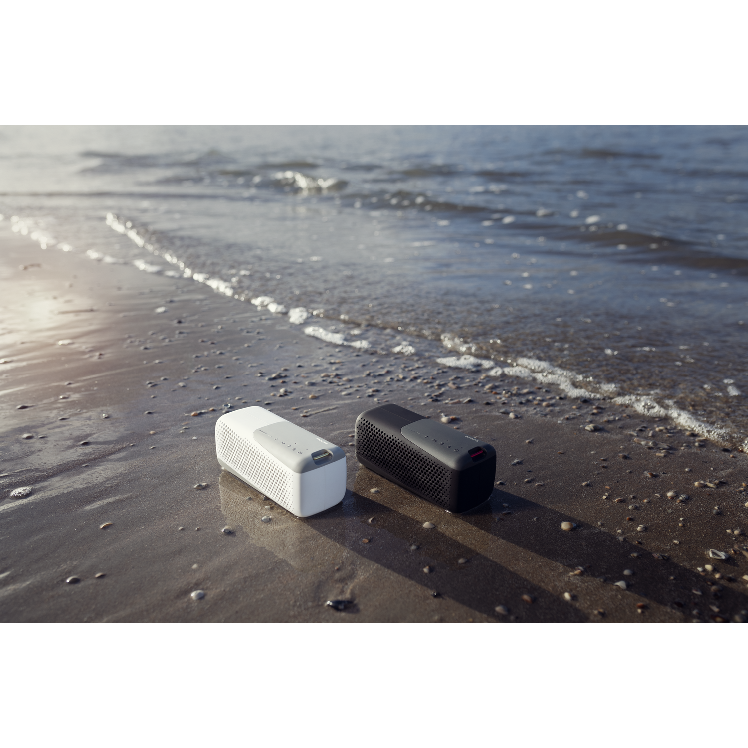 Twee witte en zwarte luidsprekers op een zandstrand bij het water.