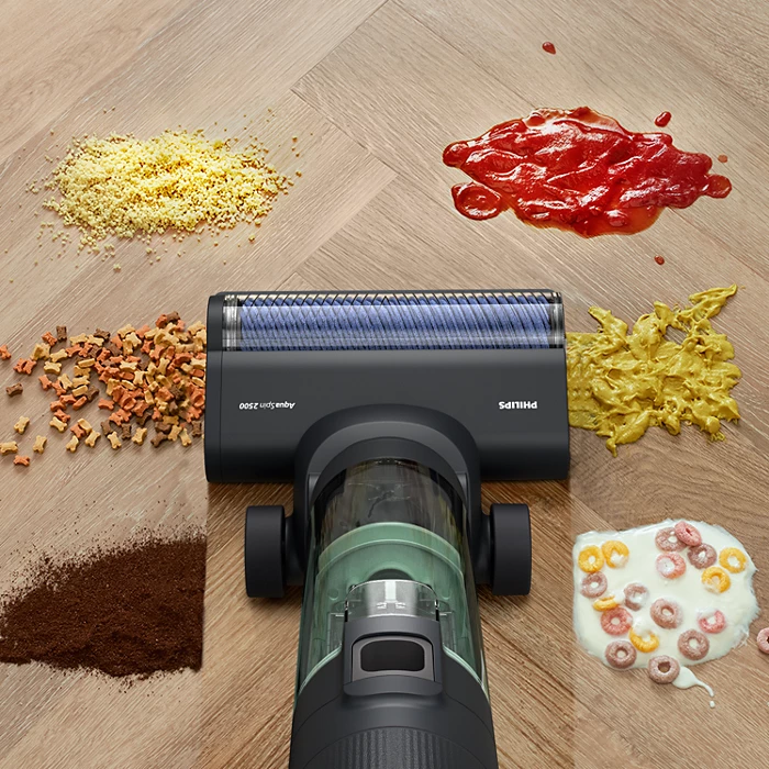 Porszívó különféle ételfoltokkal a fa padlón: morzsák, ketchup, tészta, gabonapehely, kávé.