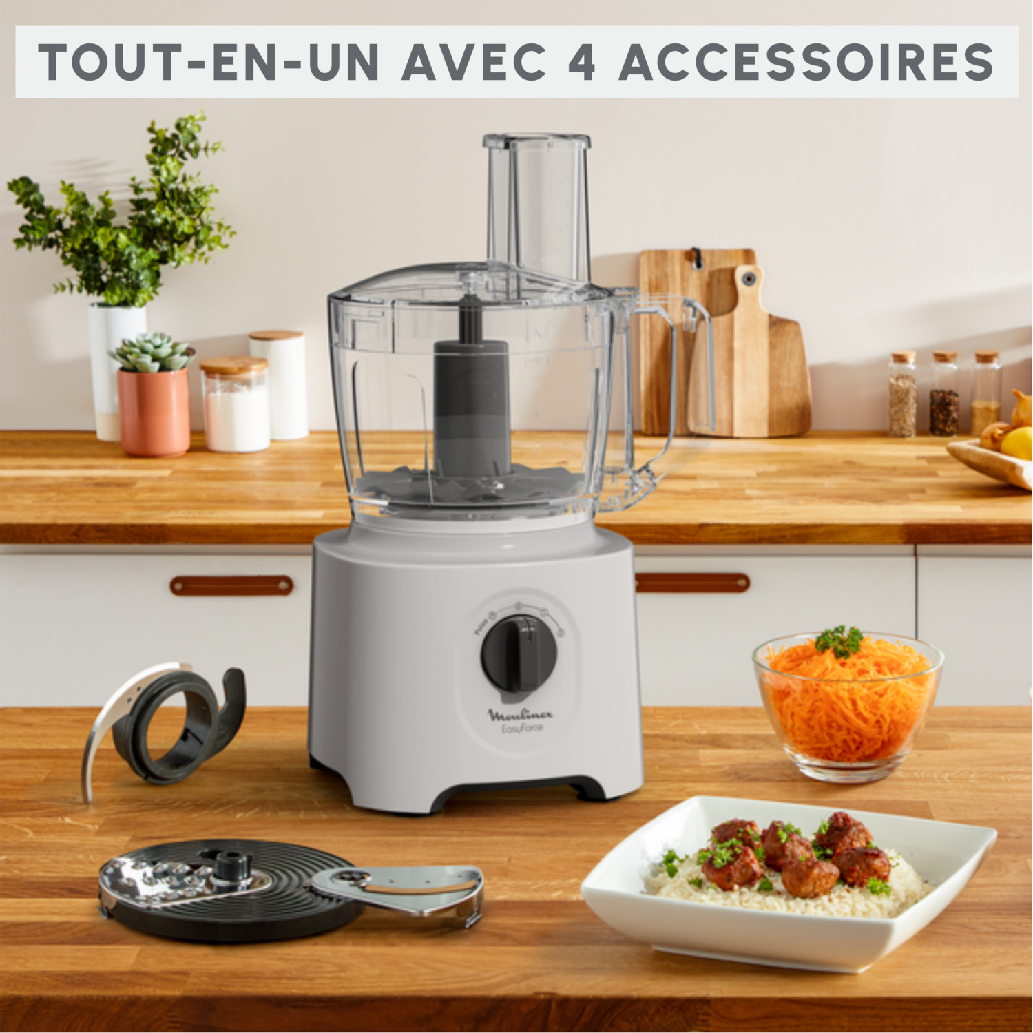 Robot culinaire avec accessoires sur un comptoir en bois, bols de carottes et boulettes de viande, et une plante verte.