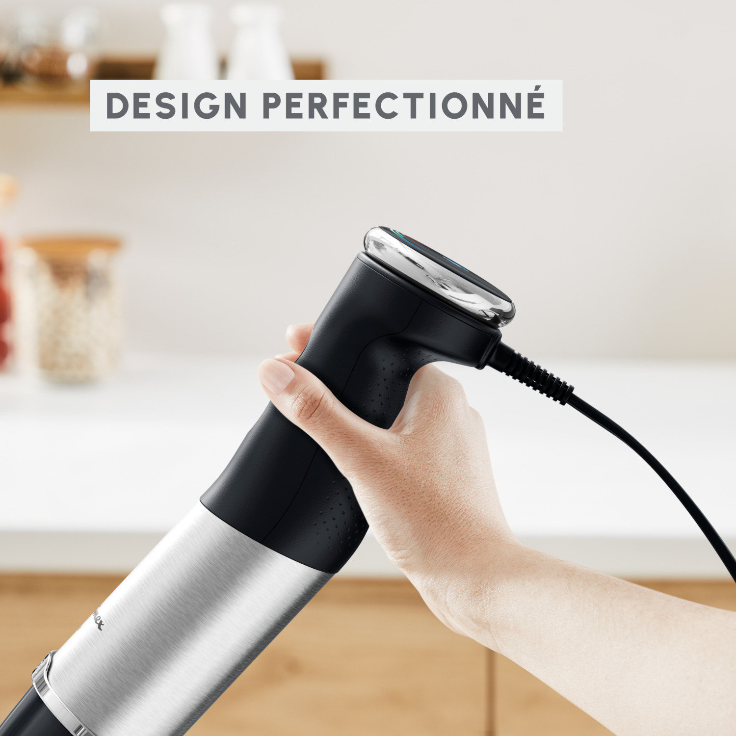 Un mixeur plongeant noir avec une base en acier inoxydable. Une main le tient.