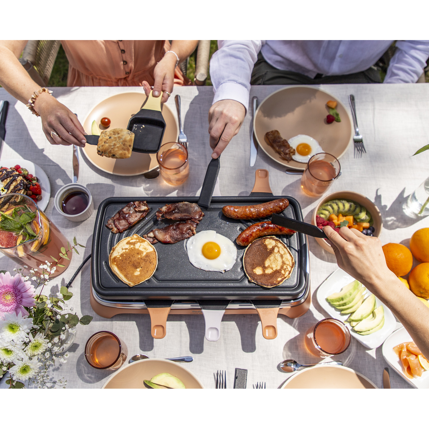 People grilling food on a raclette grill. Includes pancakes, eggs, bacon, and sausages.
