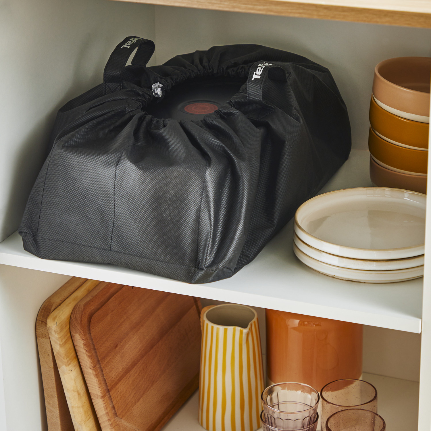 A black bag inside a white cabinet shelf, with cutting boards and plates nearby.