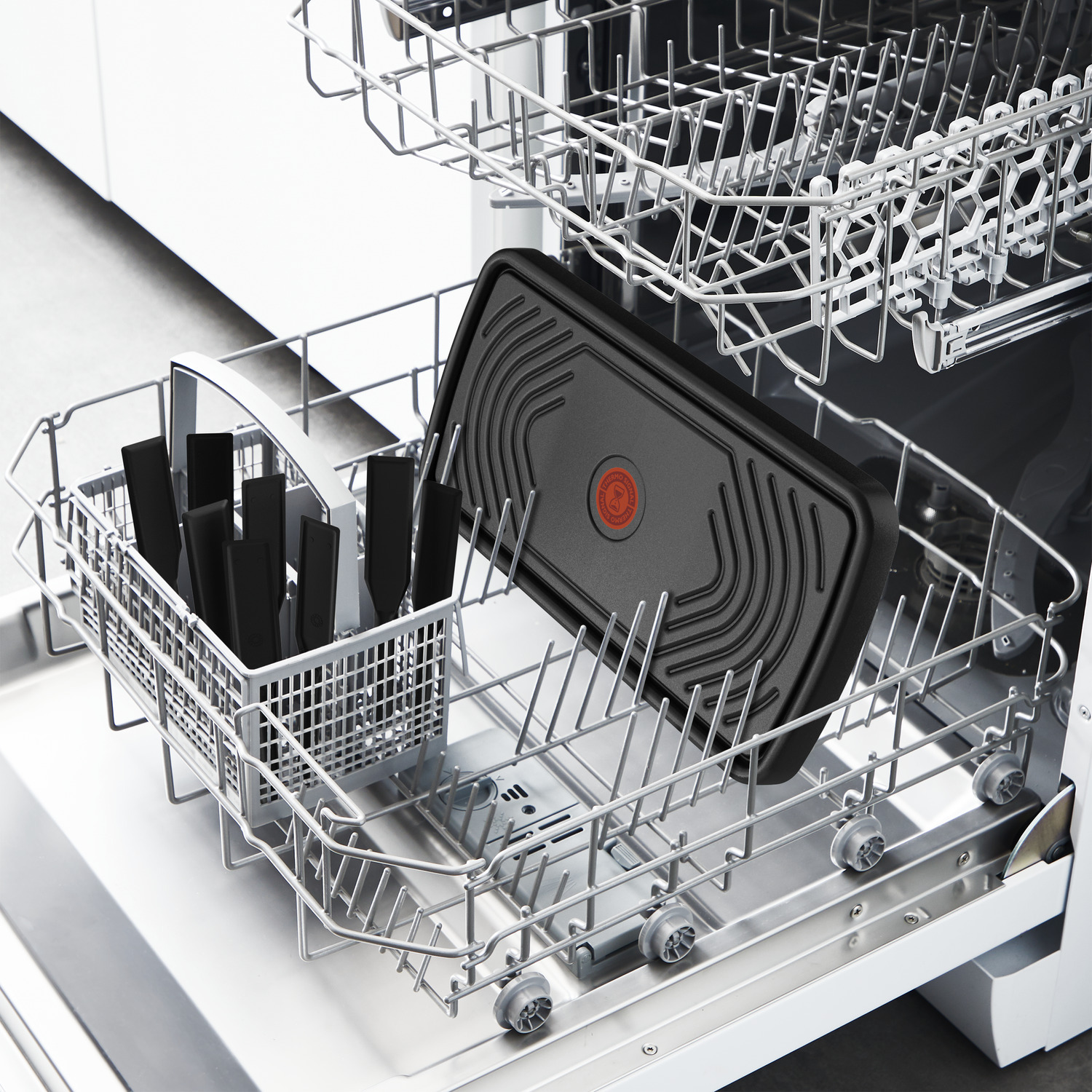 A dishwasher with a black non-stick pan, and black utensils in a basket, all on a white background.