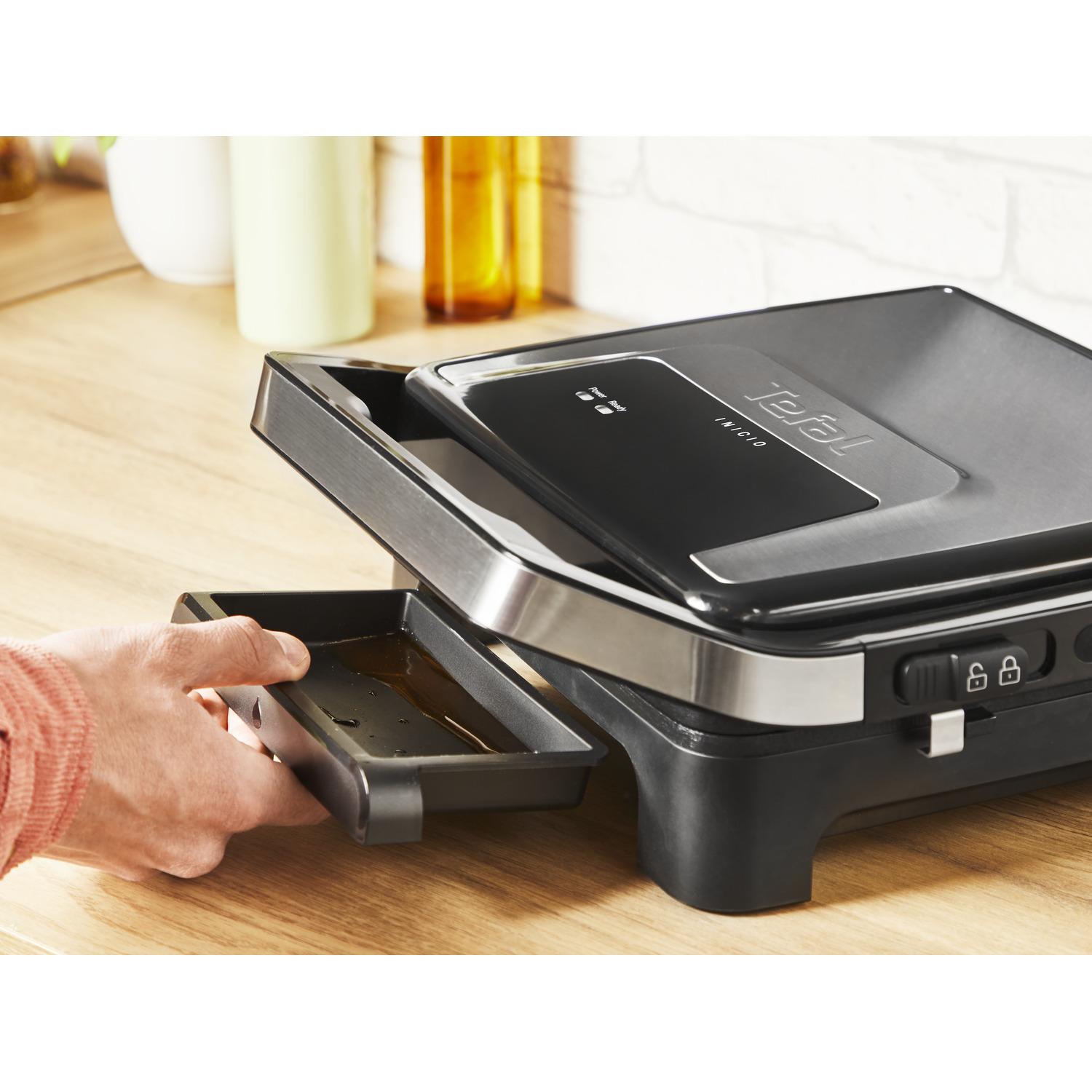 A person pulling out a tray from a black and silver Tefal grill.