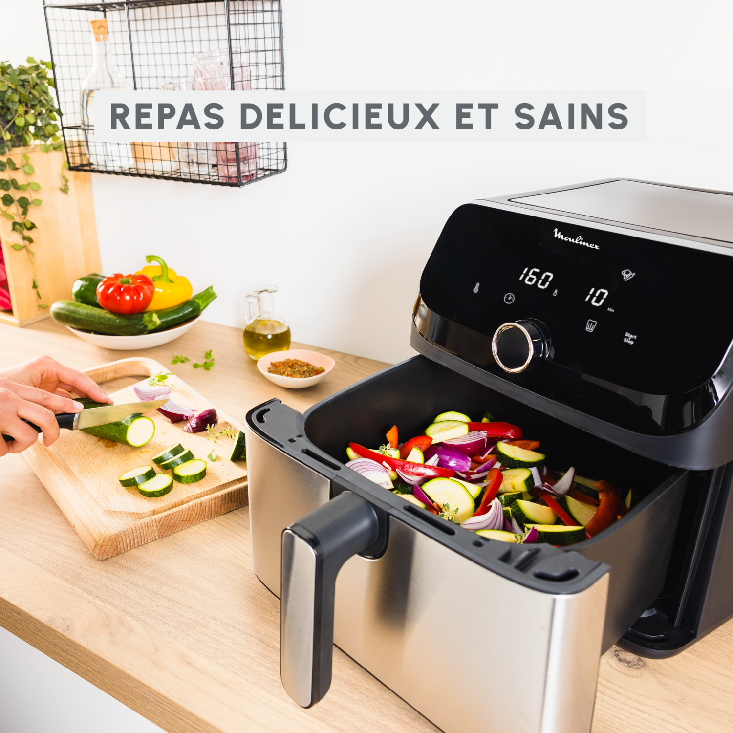 Friteuse à air avec légumes. Personne coupe courgette et oignon rouge.