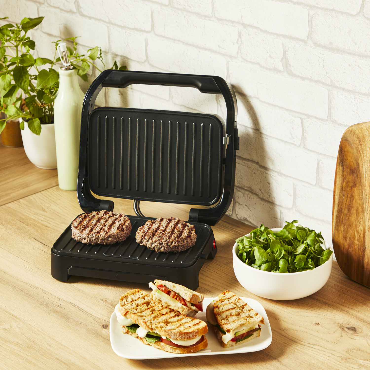 Gegrilde hamburgers en sandwiches op een grill en een bord, met salade in de buurt.