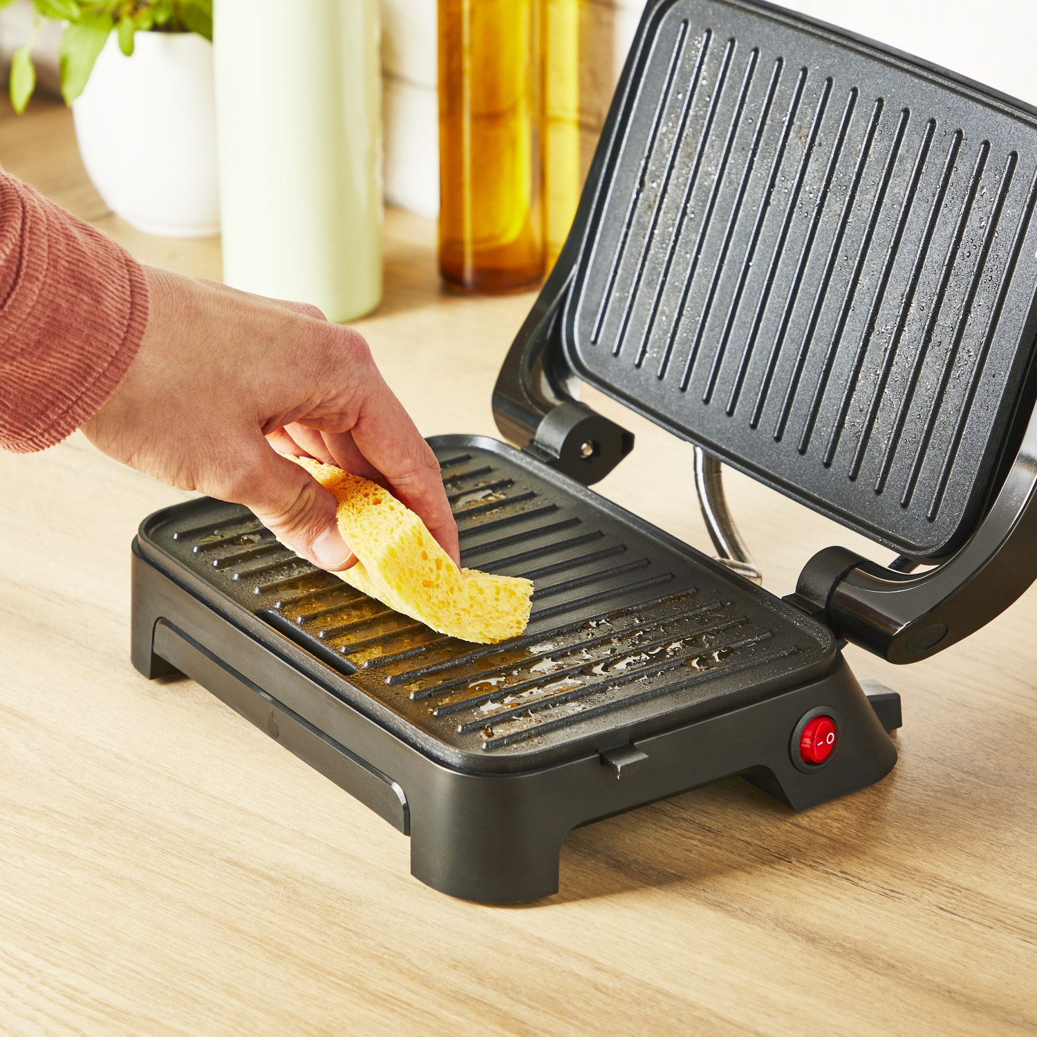 Een persoon legt een stuk brood op een zwarte grill met rode aan/uit-knop.