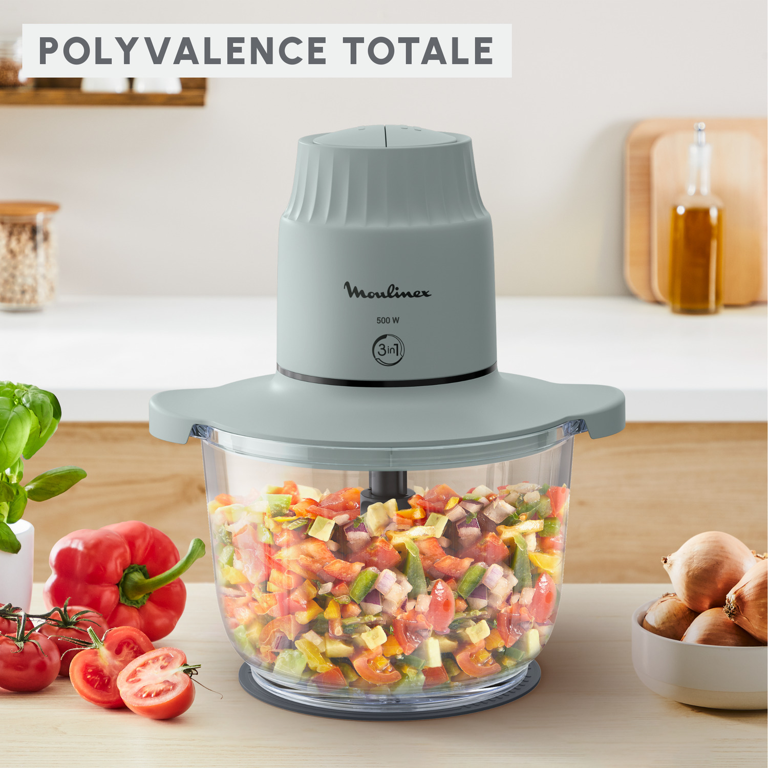 Un robot culinaire gris avec des légumes hachés à l'intérieur. Des tomates, des oignons et d'autres ingrédients sont sur la table.