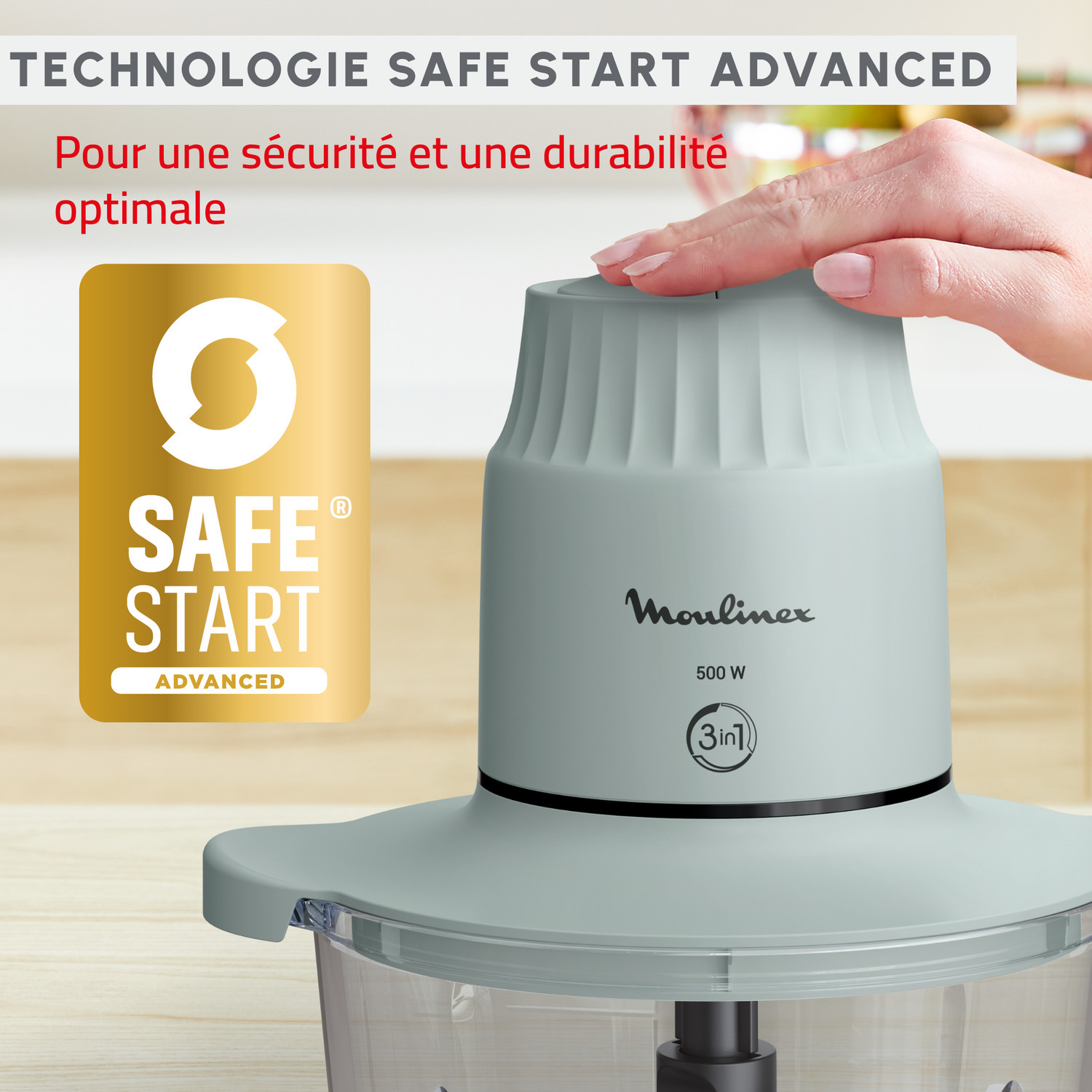 Une main touche un robot culinaire Moulinex vert clair avec un badge 'Safe Start' doré.