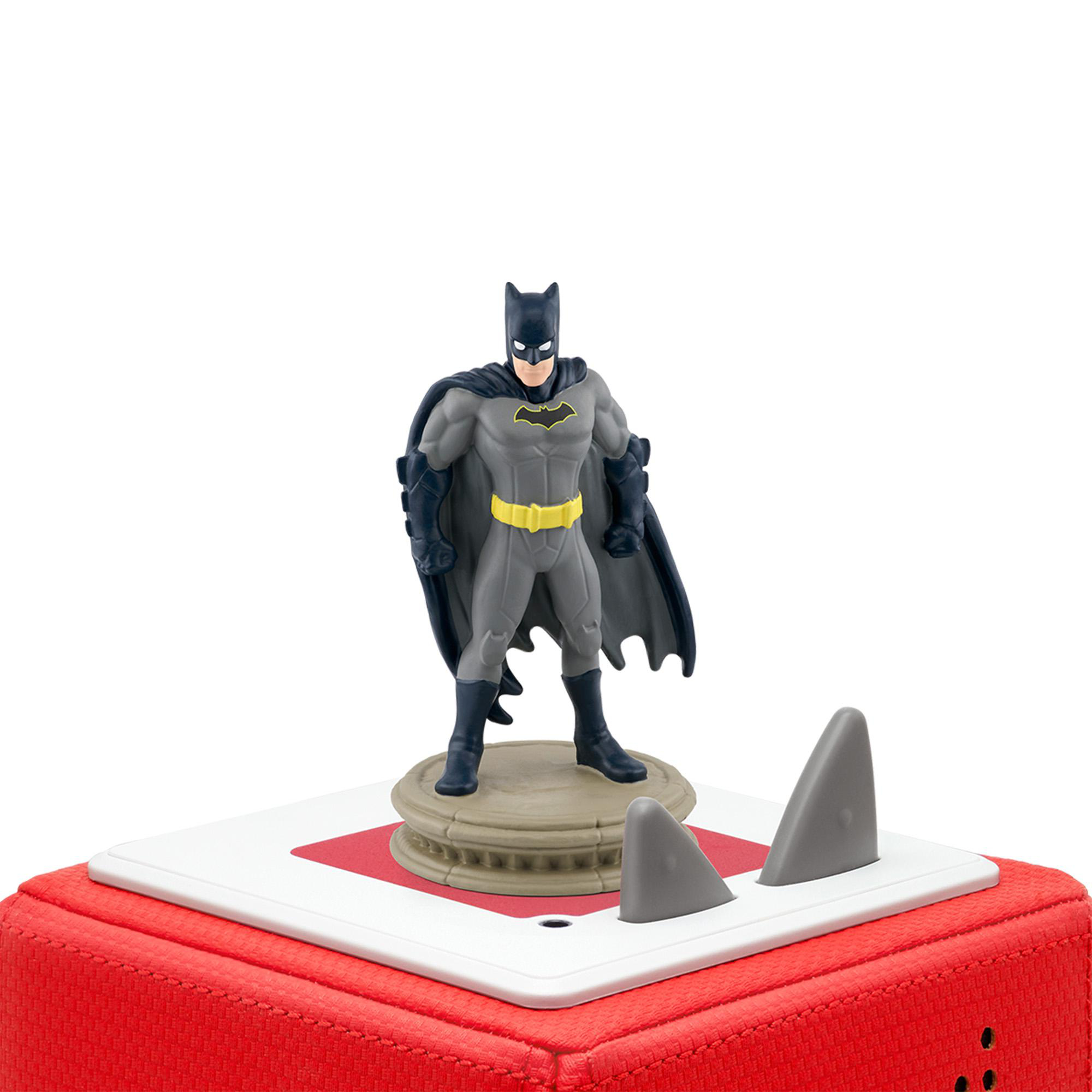 Eine Batman-Figur steht auf roter Basis mit Haifischflossen, weißer Hintergrund. Figur grau und schwarz.