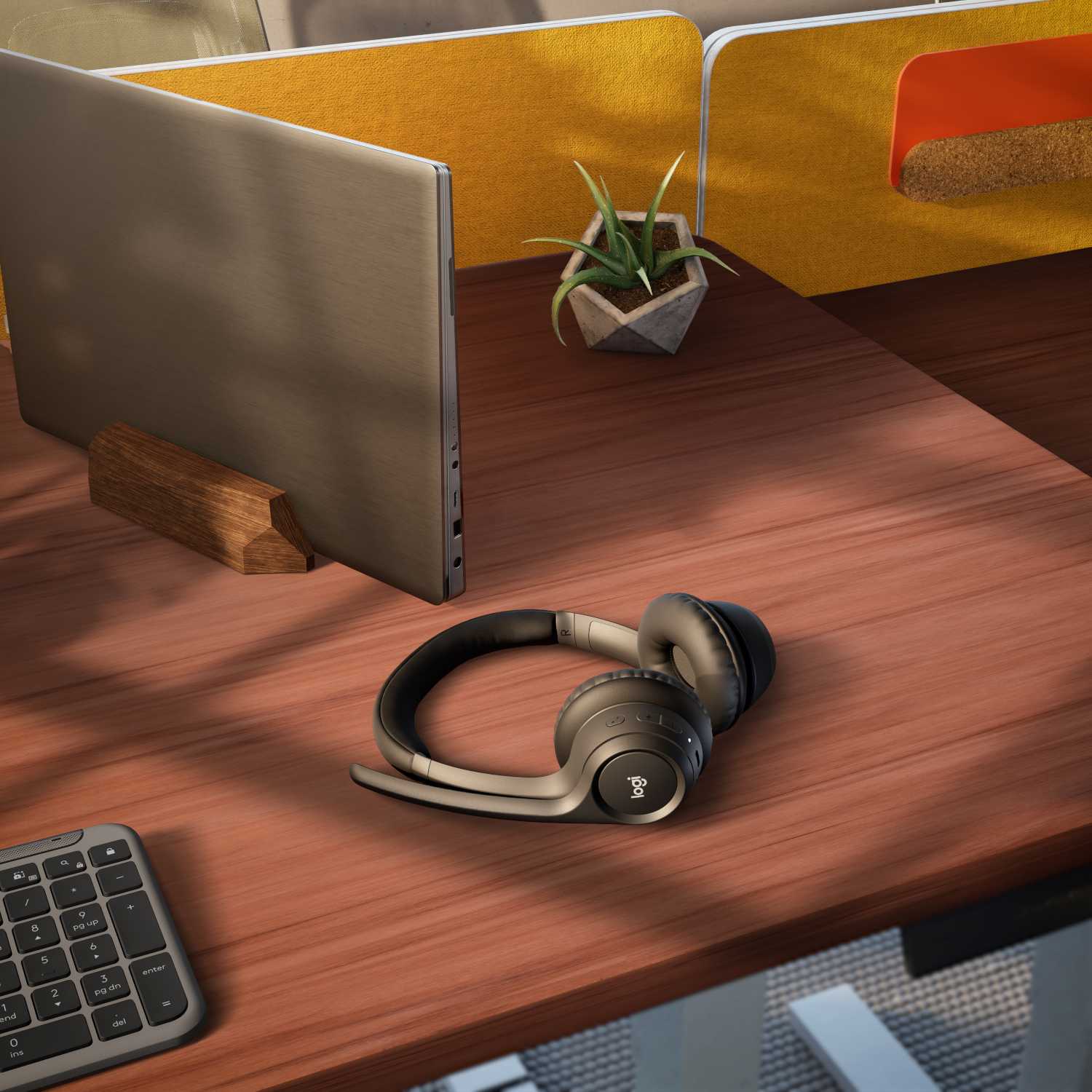 Ein Schreibtisch mit Laptop, Kopfhörern, kleiner Pflanze und Tastatur. Der Schreibtisch ist holzfarben.