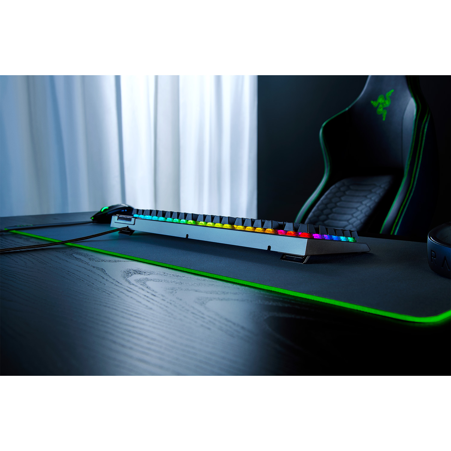 Una tastiera da gioco con luci colorate, posizionata su una scrivania con un tappetino e una sedia verdi.