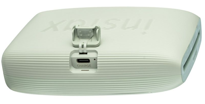 Egy Instax nyomtató közeli képe, a töltőportot és egy nyitott nyílást mutatva.