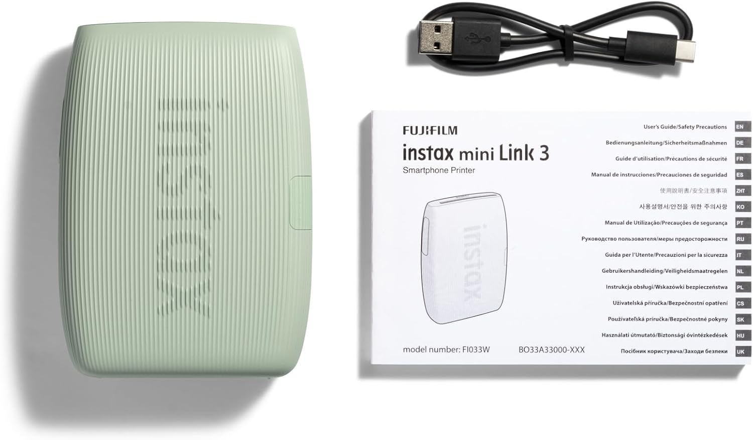 Instax Mini Link 3 nyomtató, USB kábel és kézikönyv fehér felületen. A nyomtató világoszöld.