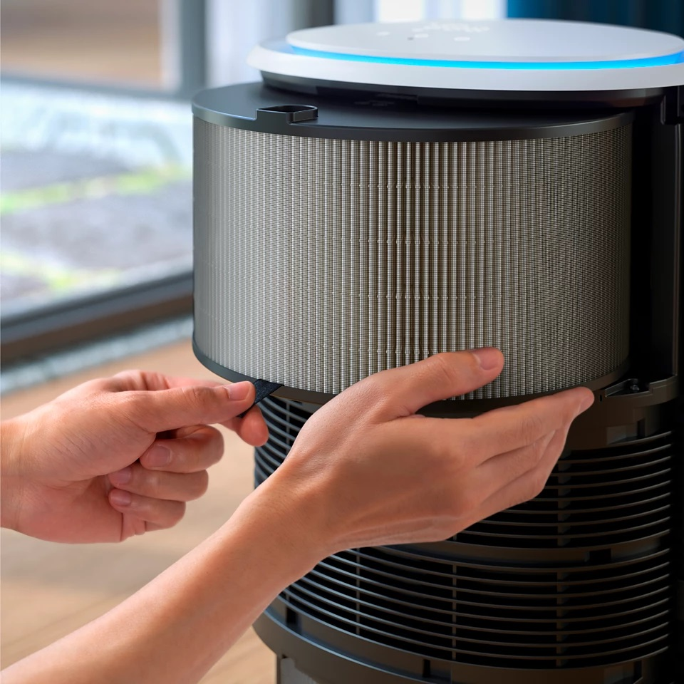 Ręce osoby wyjmującej filtr powietrza z czarno-białego oczyszczacza powietrza.