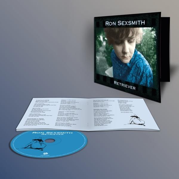 CD-Cover mit Foto eines Mannes, geöffnetem Booklet und blauer CD auf grauem Hintergrund.