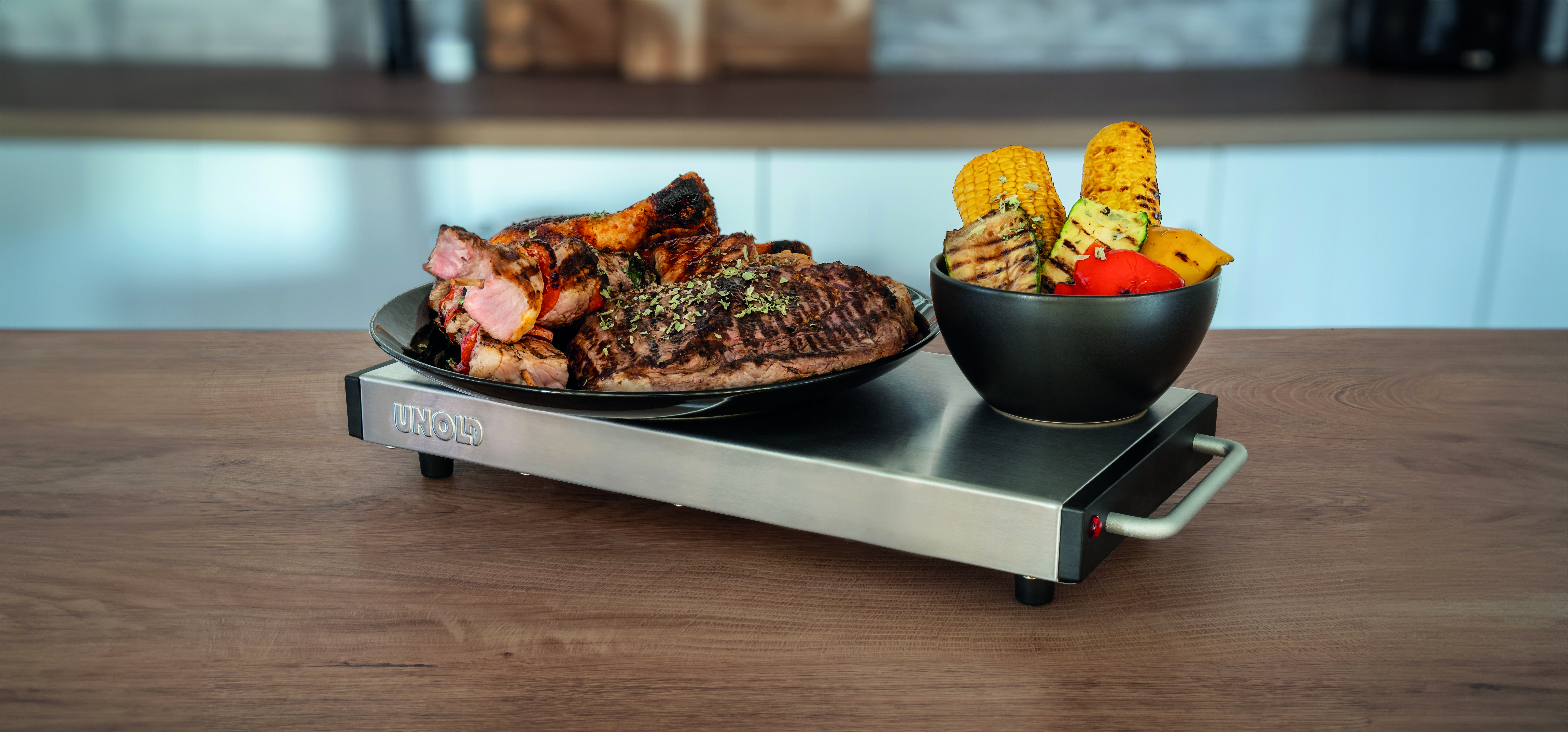 Speisenwärmer mit gegrilltem Essen und Gemüse auf einem Holztisch.