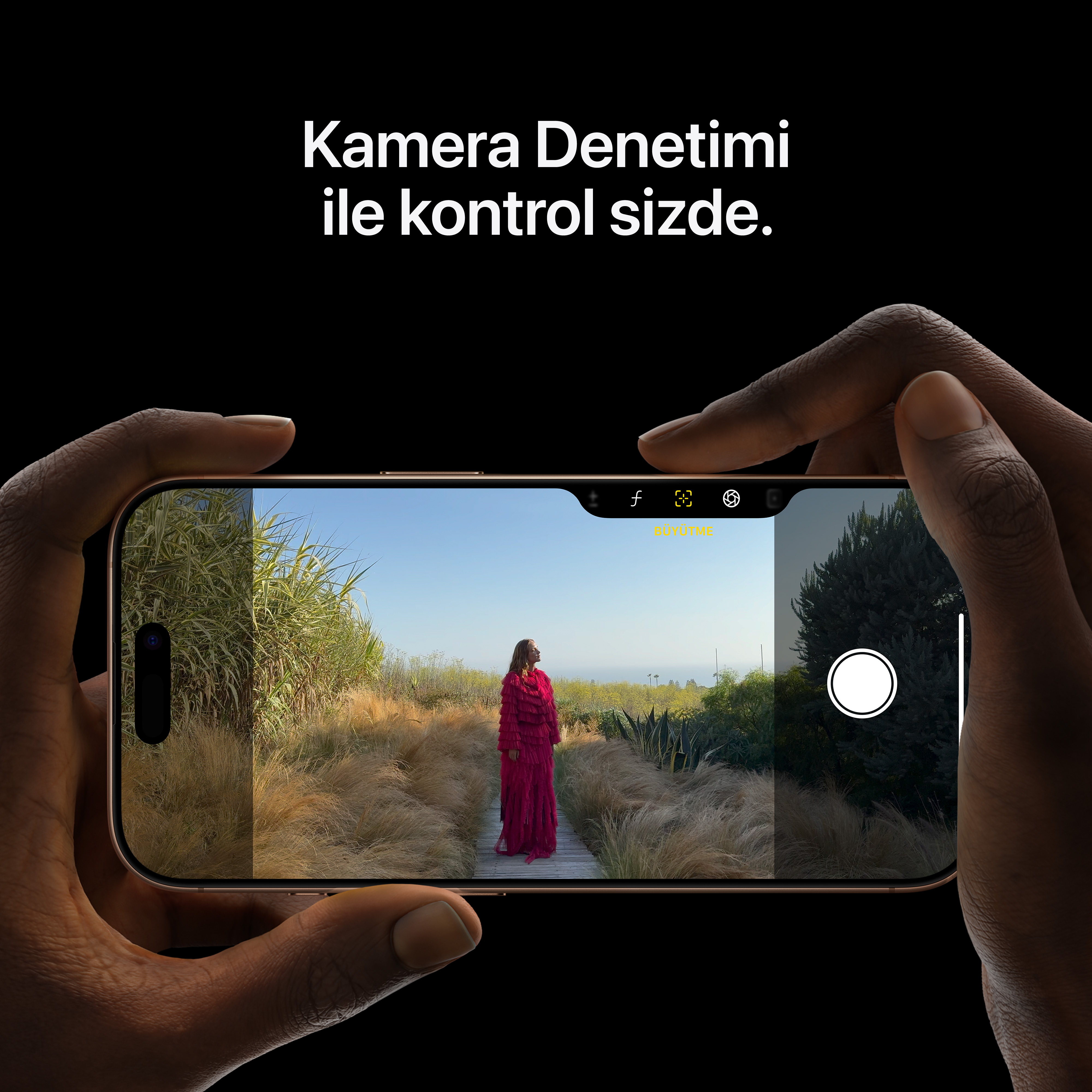 Ellerde altın bir iPhone, ekranda kırmızı giymiş bir kadın ve çevresinde bir manzara var.