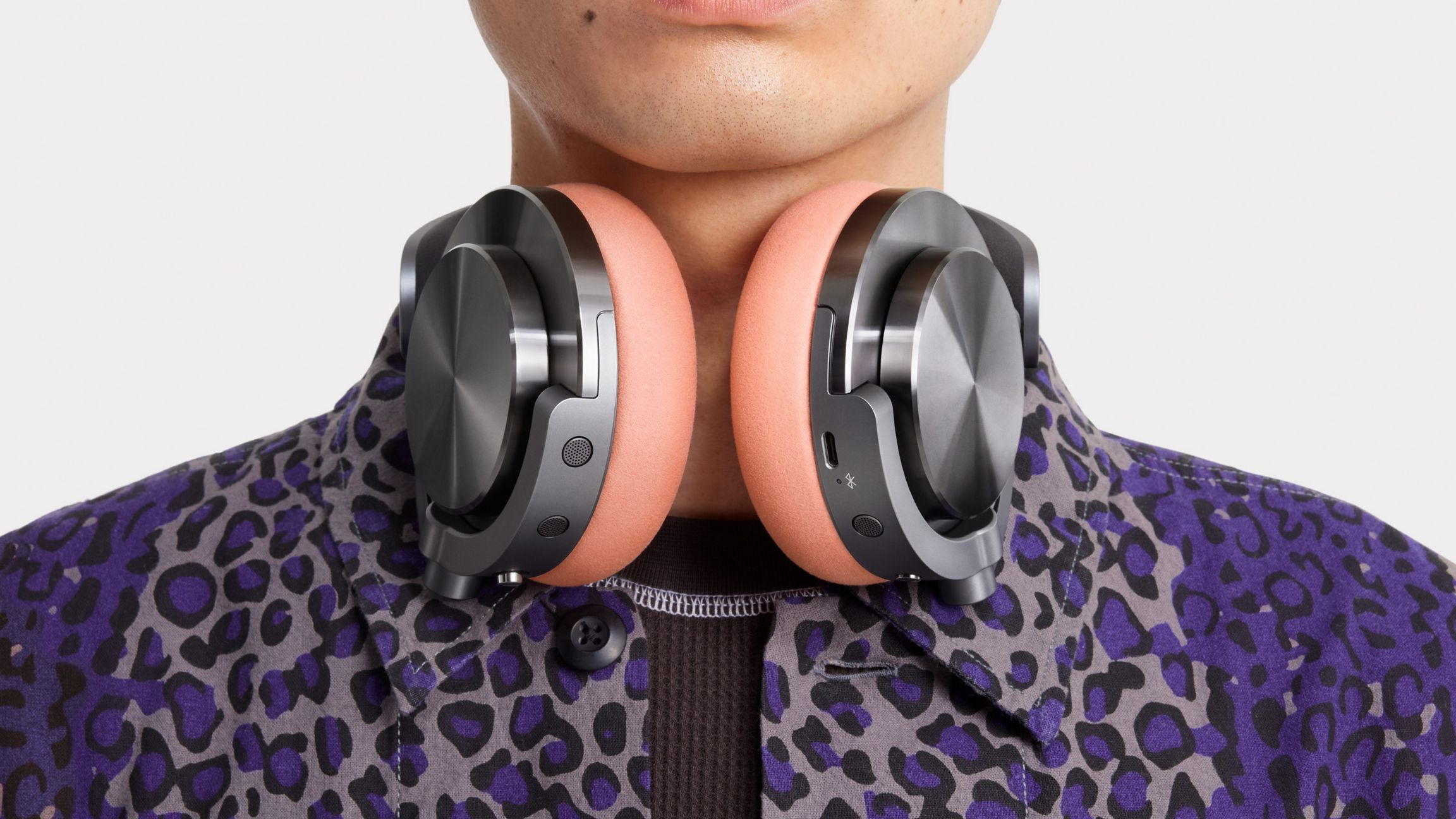 Homme portant un casque. Les coussinets sont pêche, le reste est sombre. Il porte une chemise à motifs.