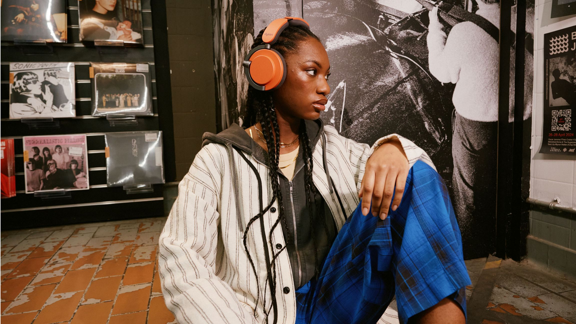 Une femme portant un casque orange, regardant ailleurs, assise dans une pièce avec des disques et des affiches.