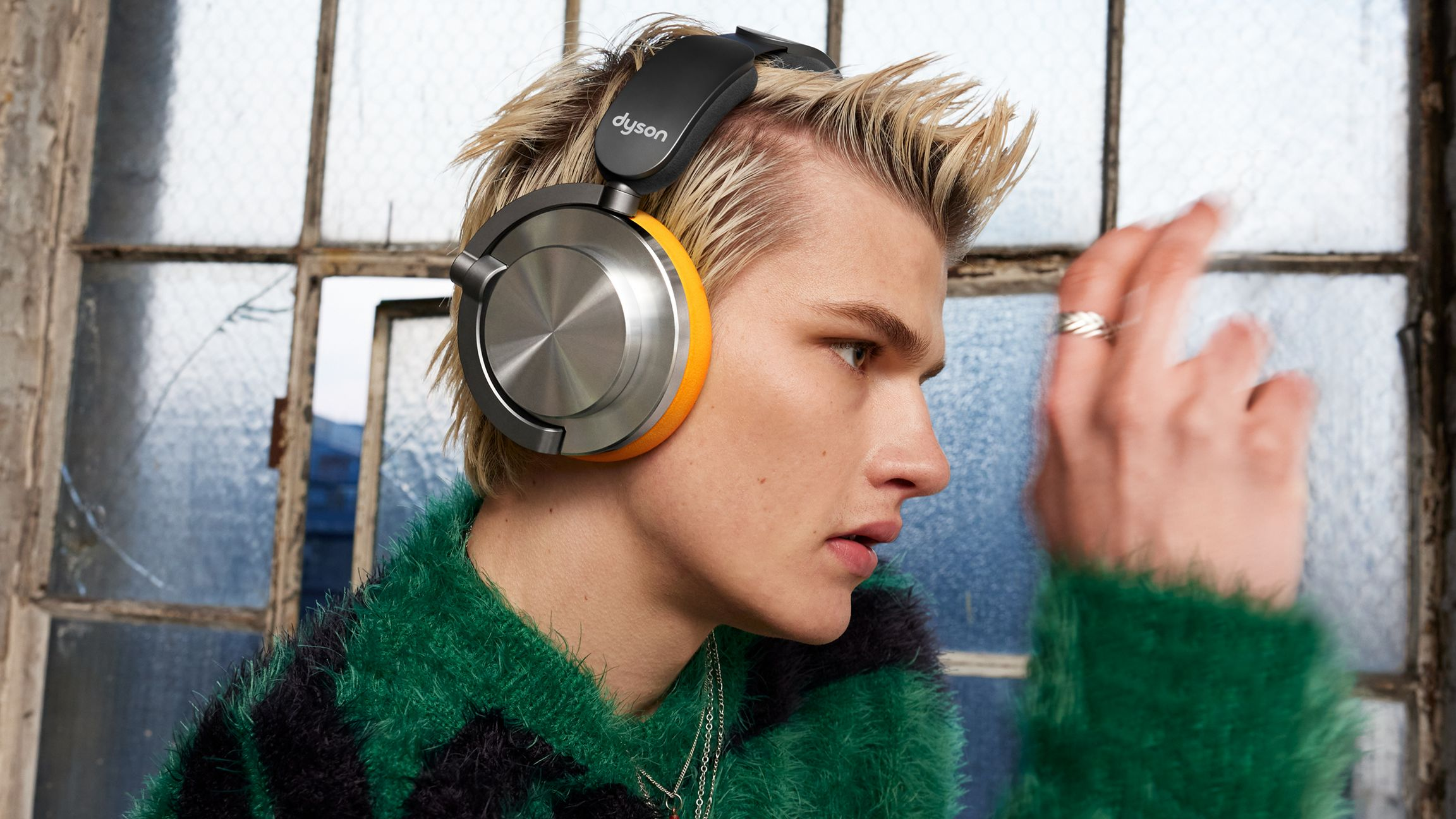 Un homme portant un casque Dyson, devant une fenêtre, avec des écouteurs oranges.