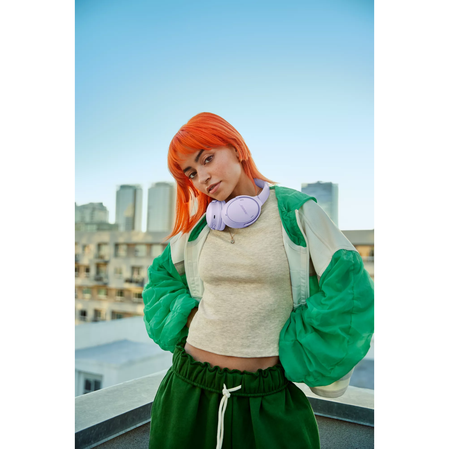 Woman with orange hair wearing headphones, looking at the camera, outdoors.