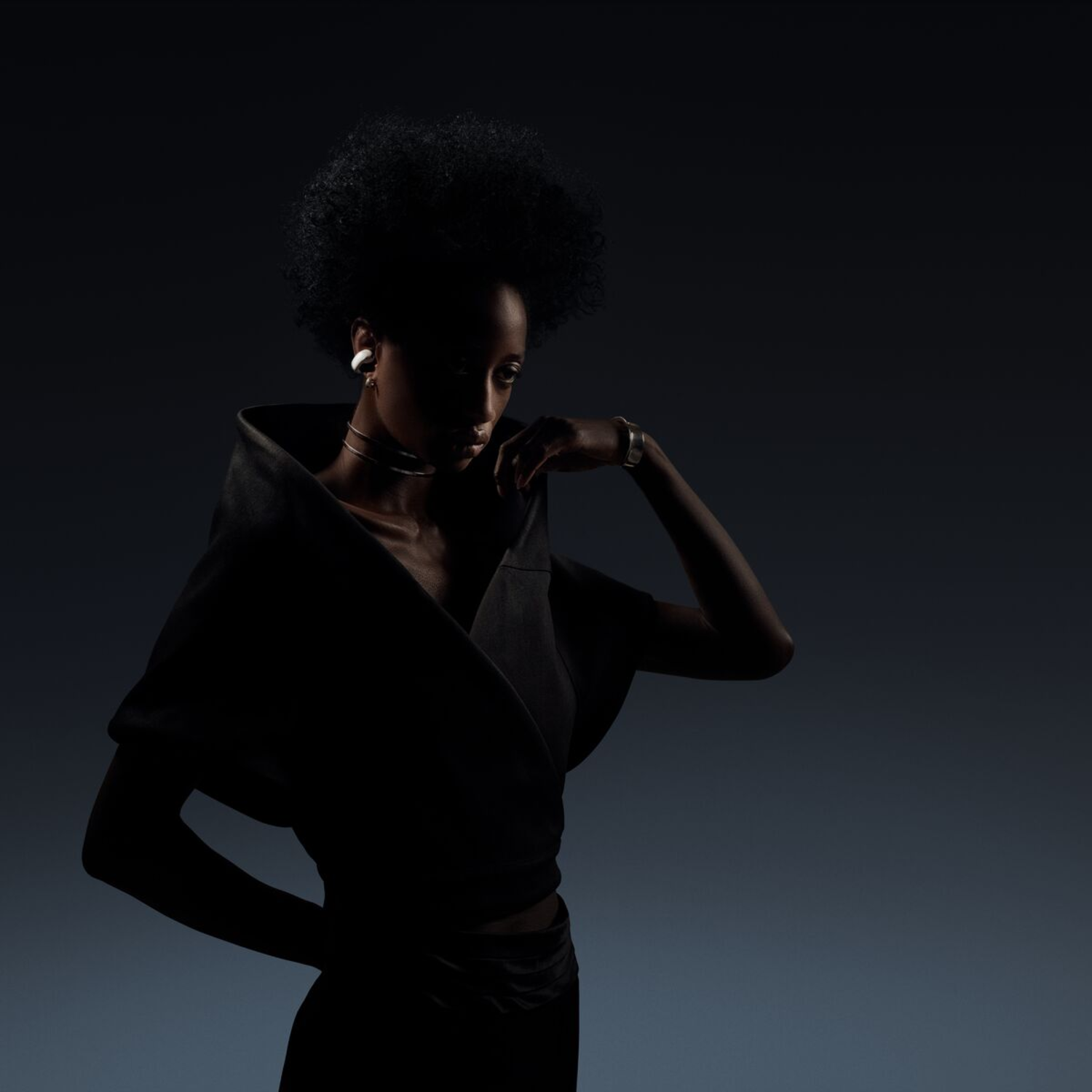 Silhouette of a woman in a dark dress, with head turned to the side, on a dark background.