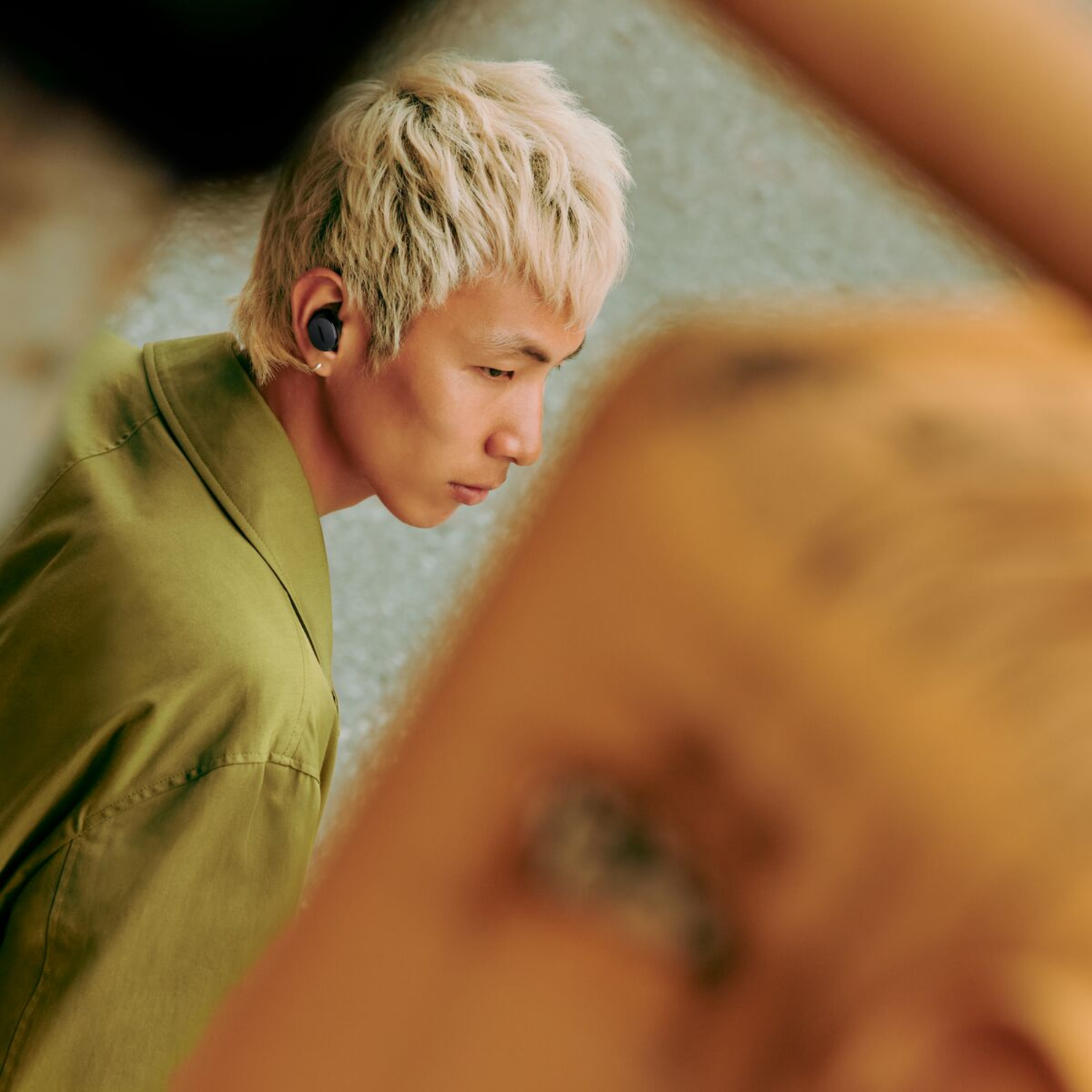 Blonde man with earbuds looking at a phone.