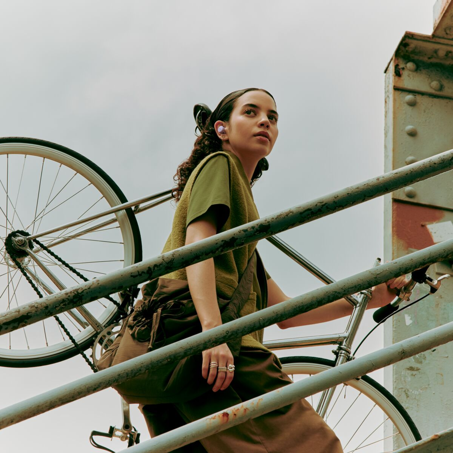 Een vrouw met oordopjes die een trap oploopt met een fiets op haar schouder, in een stedelijke omgeving.